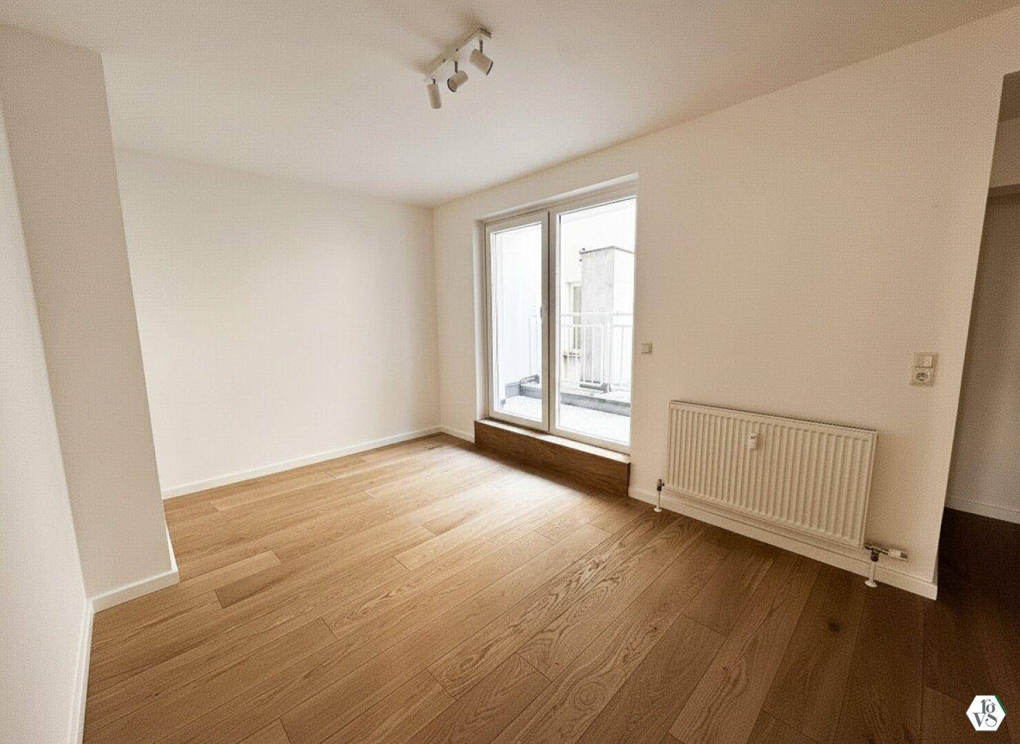 Helles Zimmer mit Holzboden und Zugang zu einem kleinen Balkon, ideal als Schlaf- oder Arbeitszimmer.