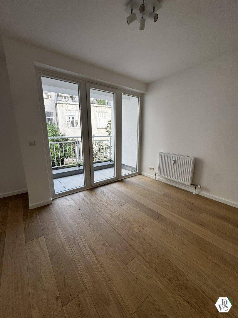 Lichtdurchfluteter Raum mit Parkettboden und Blick auf die gegenüberliegenden Gebäude vom Balkon.