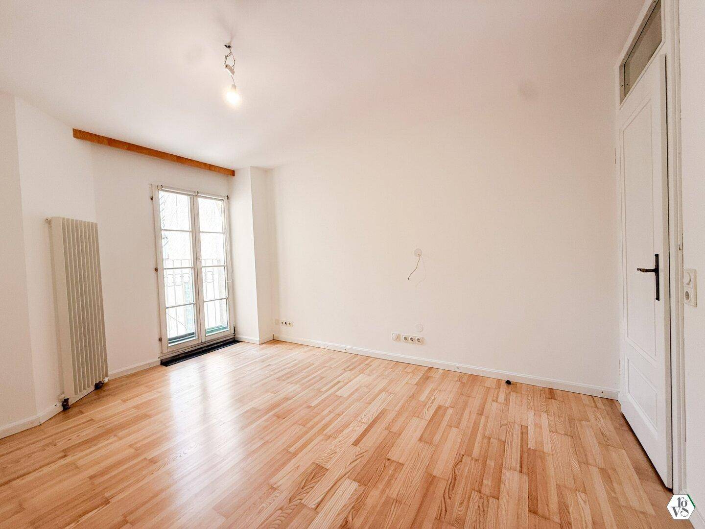 Zimmer mit hellem Holzboden, weiß gestrichenen Wänden und einem französischen Balkon.