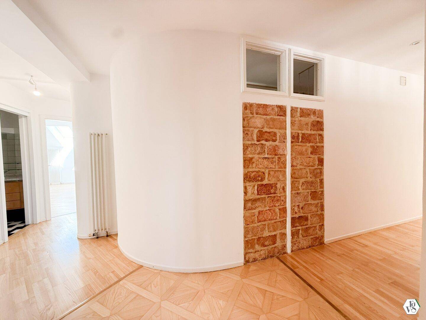 Heller Flur mit Parkettboden, einer geschwungenen Wand und dekorativen Ziegelakzenten.