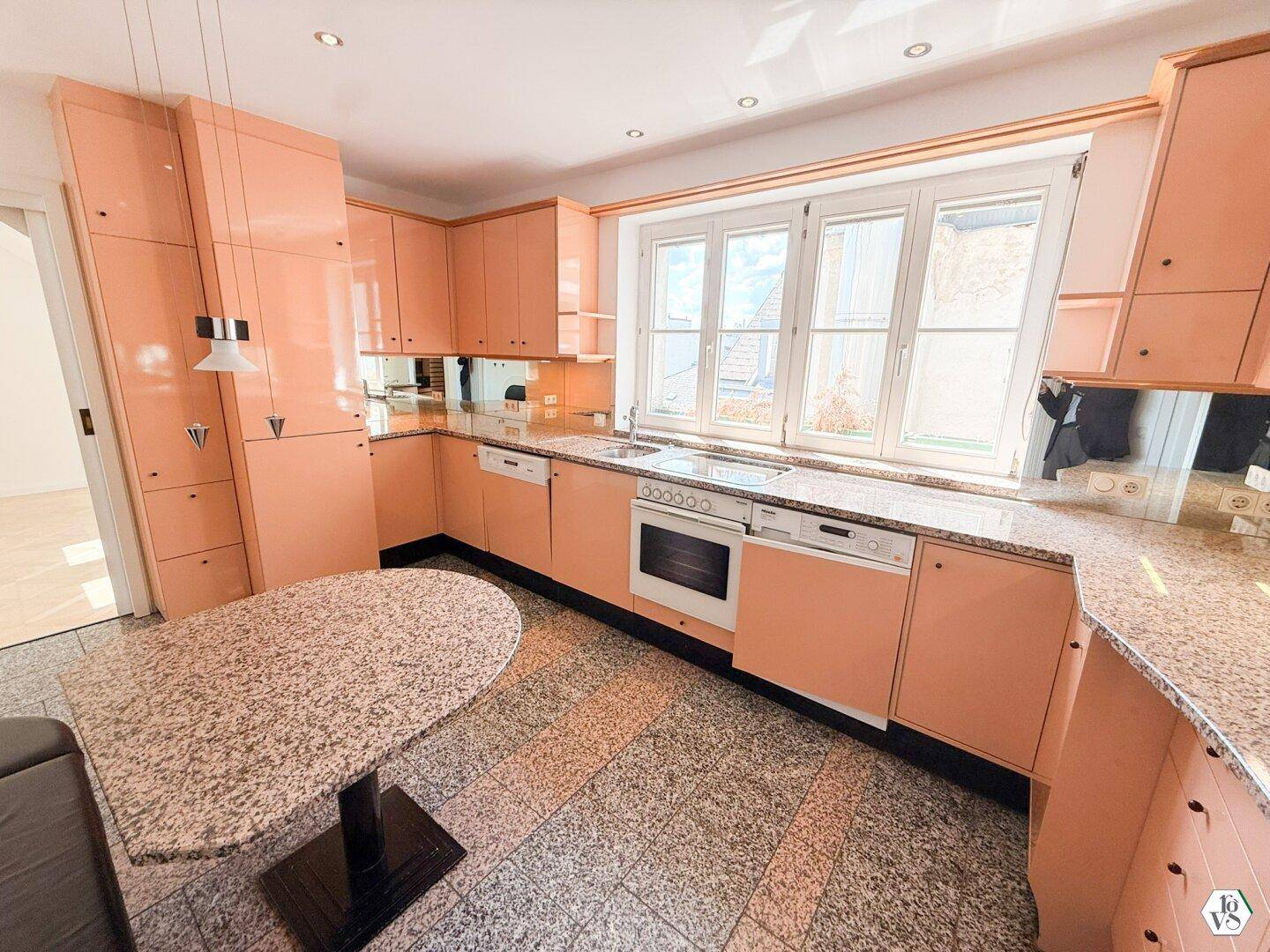 Küche im 80er-Jahre-Stil mit pfirsichfarbenen Schränken, Granitarbeitsplatten und Essbereich am Fenster.