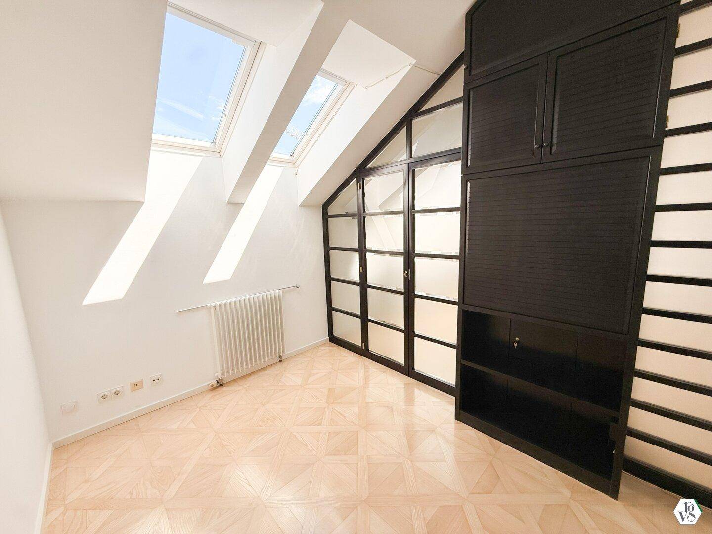 Dachzimmer mit schrägen Wänden, integriertem Schrank und mehreren Dachfenstern für viel Helligkeit.