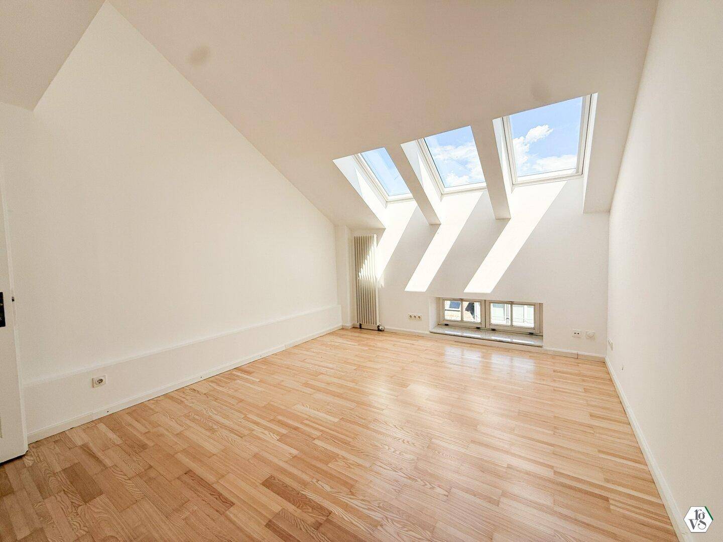 Lichtdurchflutetes Zimmer mit Holzboden, schrägen Wänden und einer Kombination aus Dach- und Normalfenstern.