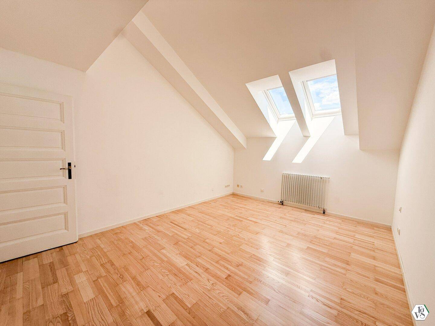 Helles Schlafzimmer im Dachgeschoss mit Holzboden, schrägen Wänden und zwei Dachfenstern.