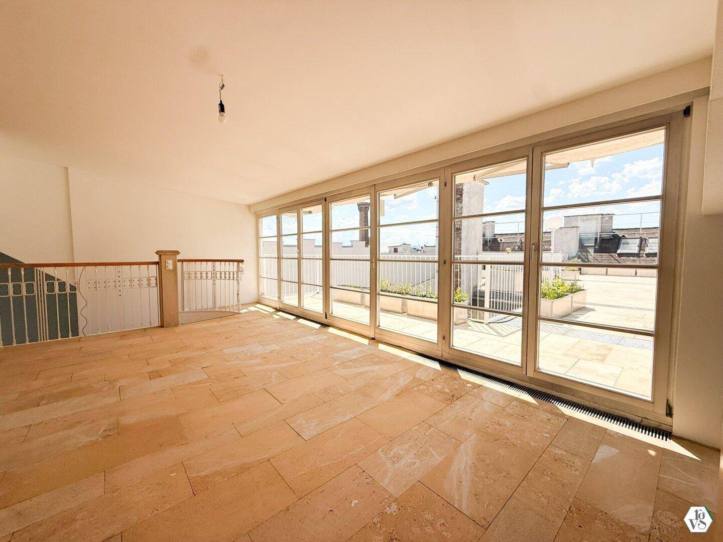 Heller Wohnraum mit Steinfliesenboden und großen Glasfronten, die Zugang zur Dachterrasse bieten.