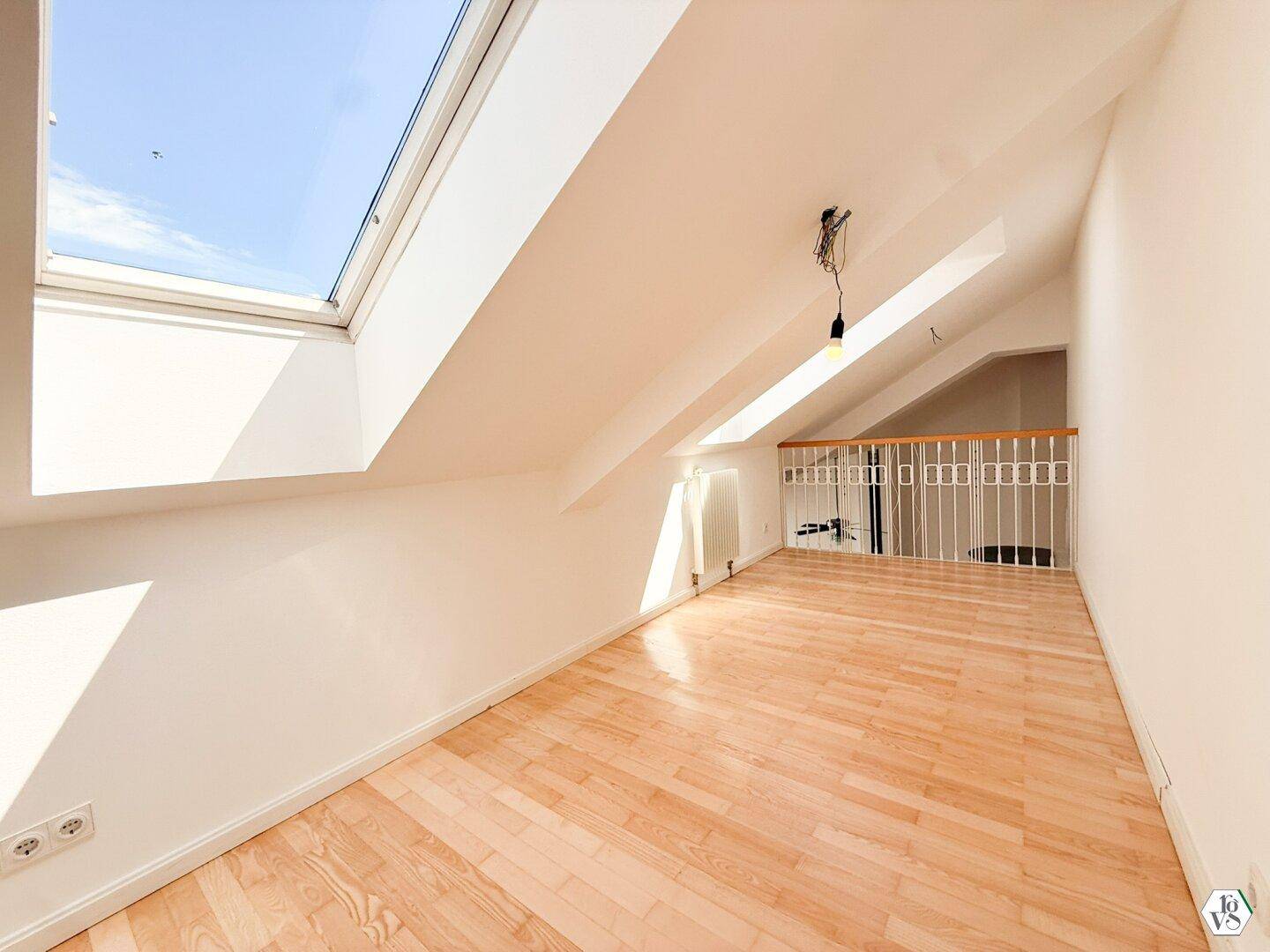 Helles Dachzimmer mit Holzboden, großem Dachfenster und einer Galeriebrüstung.
