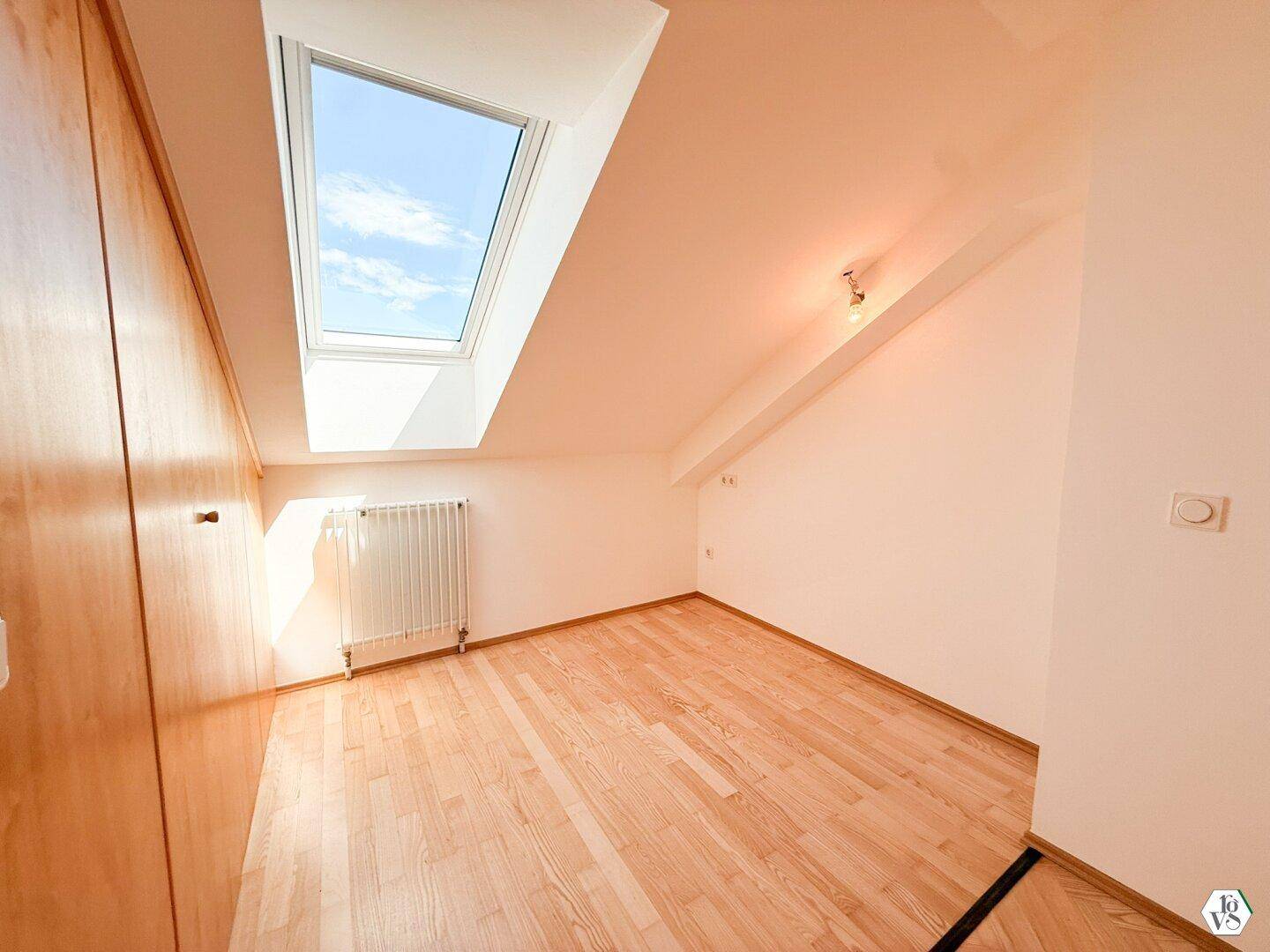 Dachzimmer mit Holzboden, Einbauschrank und einem großen Dachfenster, das viel Licht spendet.