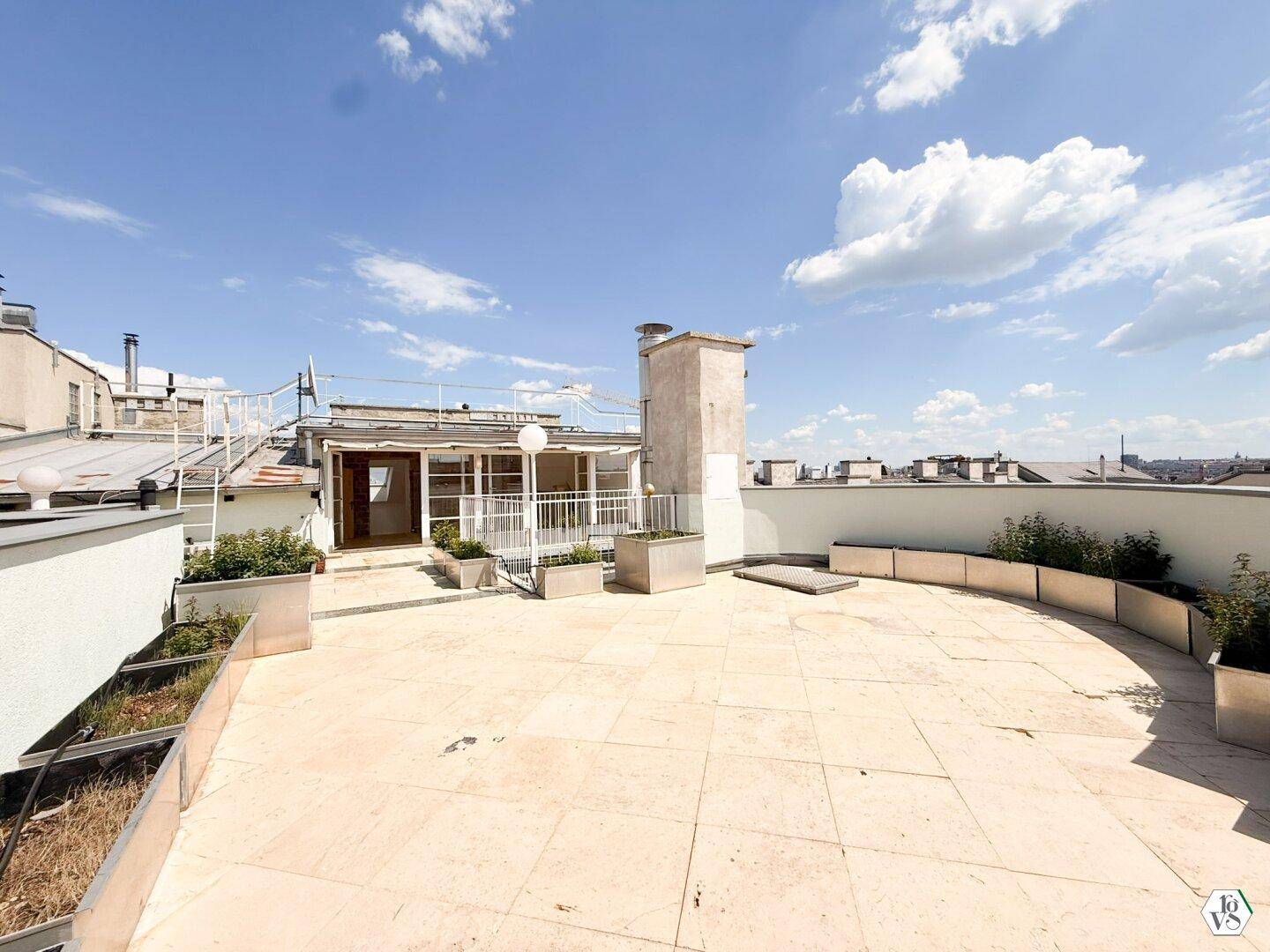 Weitläufige Dachterrasse mit hellen Fliesen, Pflanzenkübeln und Panoramablick über die Stadt.