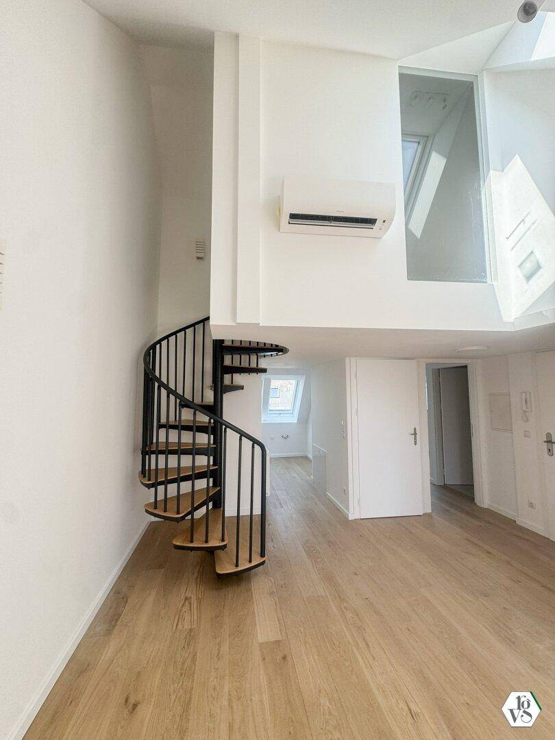 Geräumiger Wohnbereich mit eleganter Wendeltreppe, Holzboden und Klimaanlage für Komfort.