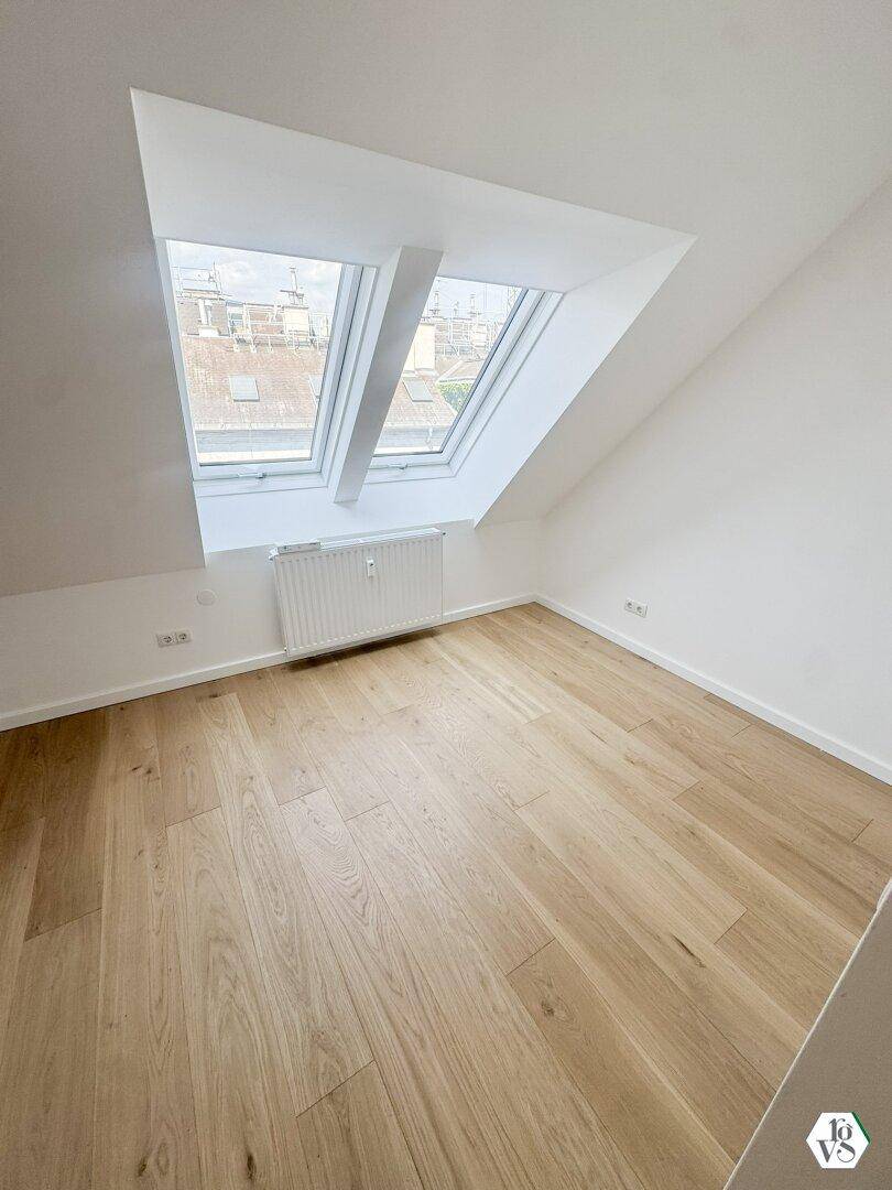 Helles Dachzimmer mit Holzboden und zwei Dachfenstern, die viel Tageslicht hereinlassen.