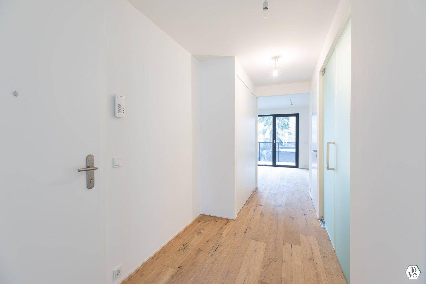 Heller Flur mit Holzboden und moderner Glastür, die zu weiteren Räumen führt.
