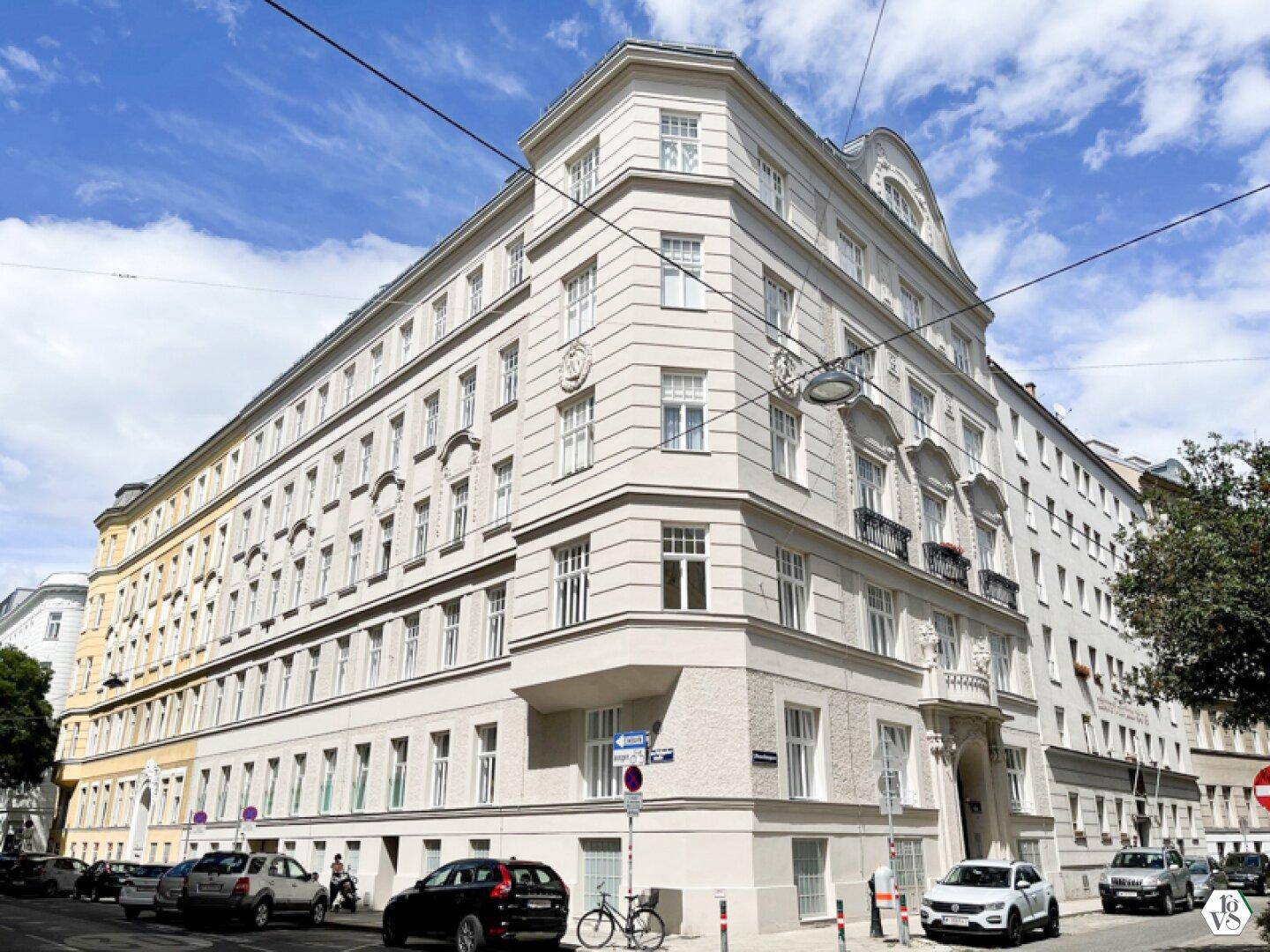 Großes, elegantes Eckgebäude mit klassischer Architektur und vielen Fenstern unter blauem Himmel.