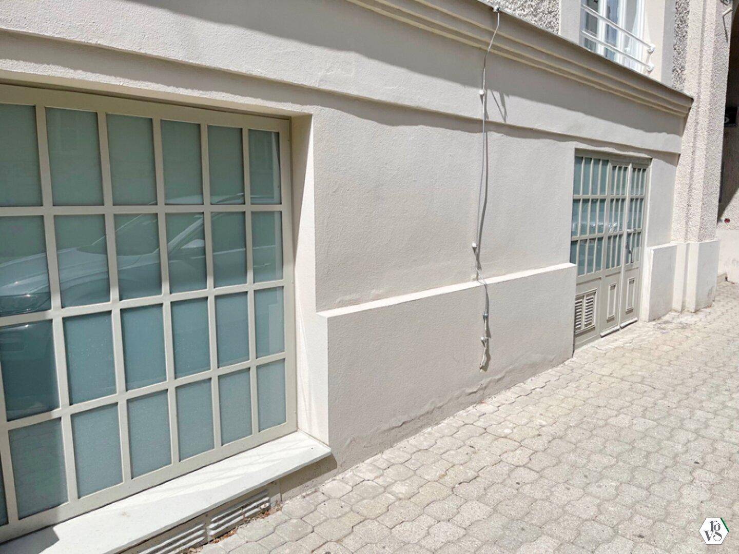Fassadenansicht des Erdgeschosses mit großen Fenstern und einer Tür, die auf einen gepflasterten Gehweg führt.