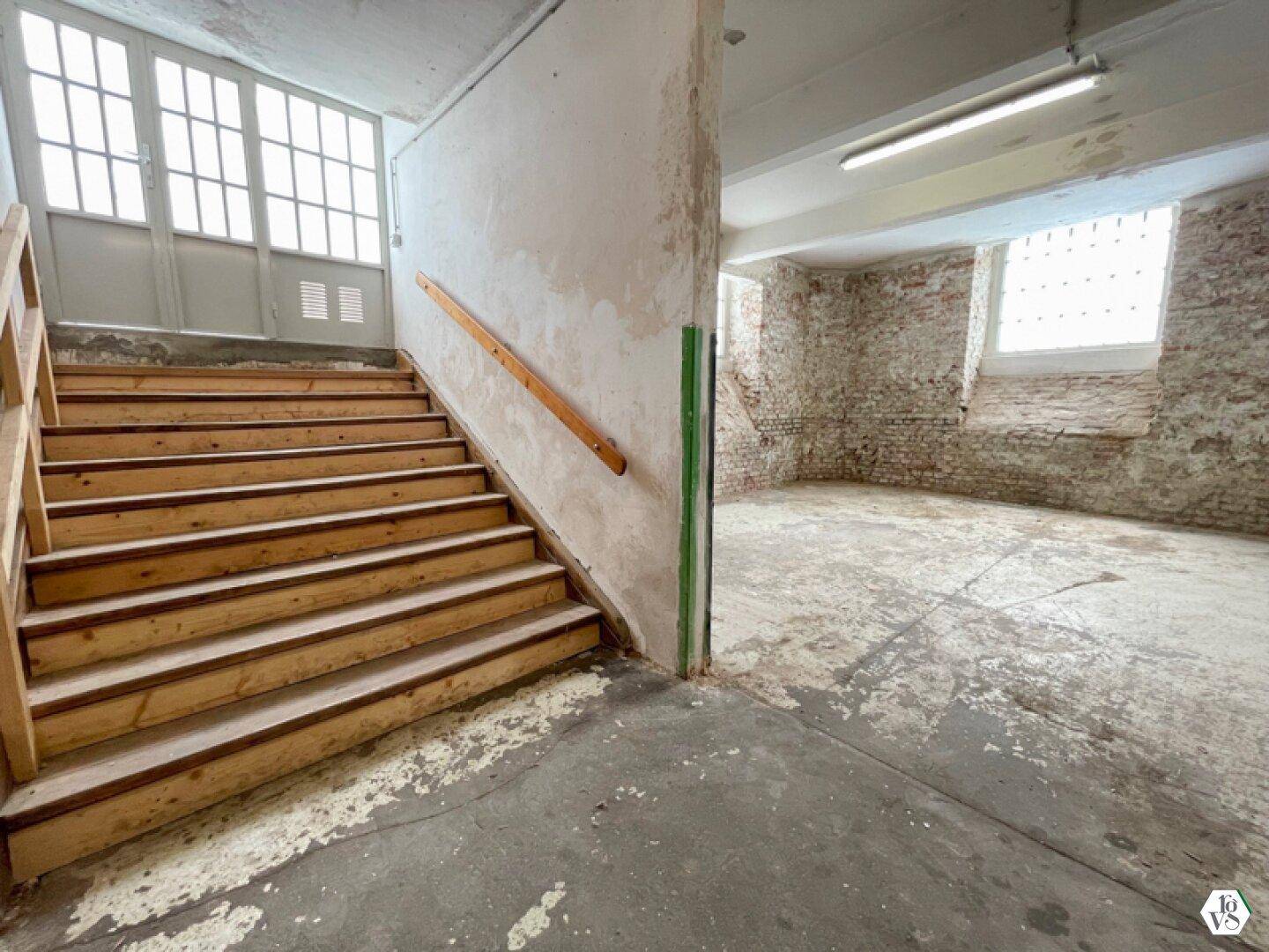 Holztreppe führt zu einer Tür mit Glaspaneelen, angrenzend an den großen Raum mit Ziegelwänden.