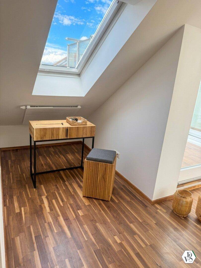 Kleiner Arbeitsbereich unter einem großen Dachfenster mit Holztisch und Hocker, sehr hell.