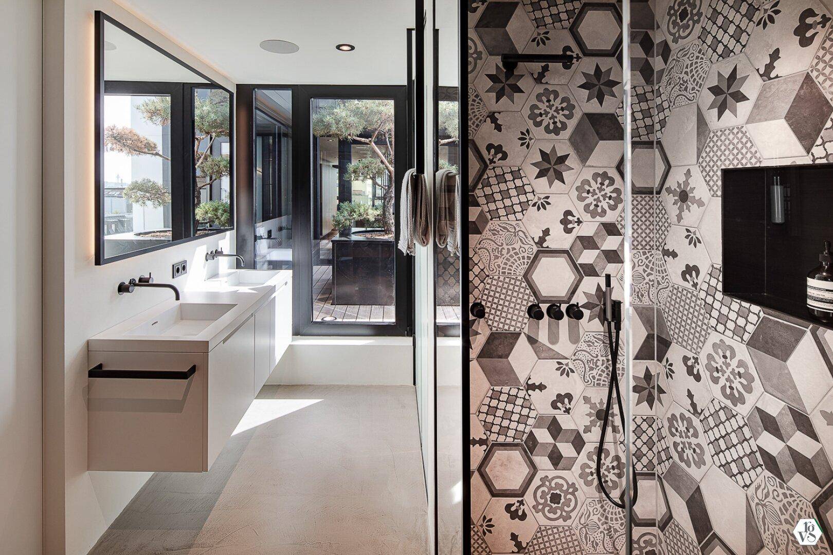 Modernes Badezimmer mit gemusterten Fliesen in der Dusche und Doppelwaschbecken.