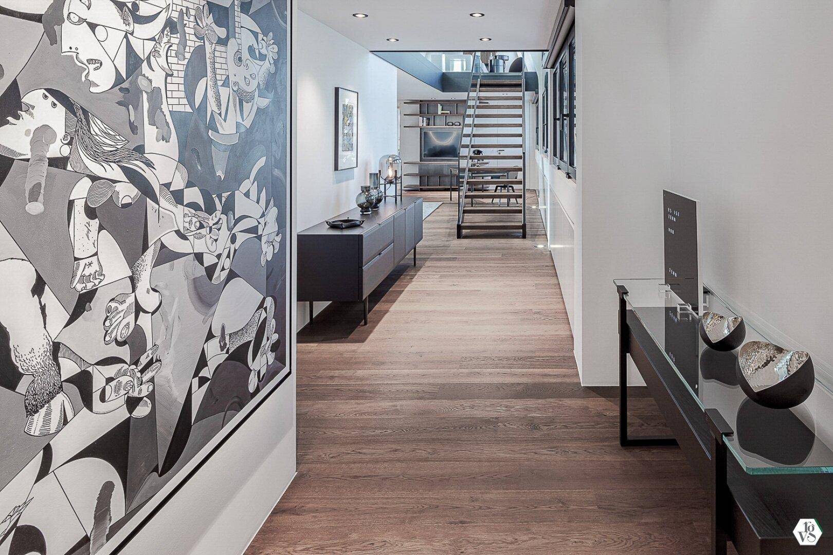 Moderner Flur mit Holzboden, Kunstwerk und Blick auf die Treppe.