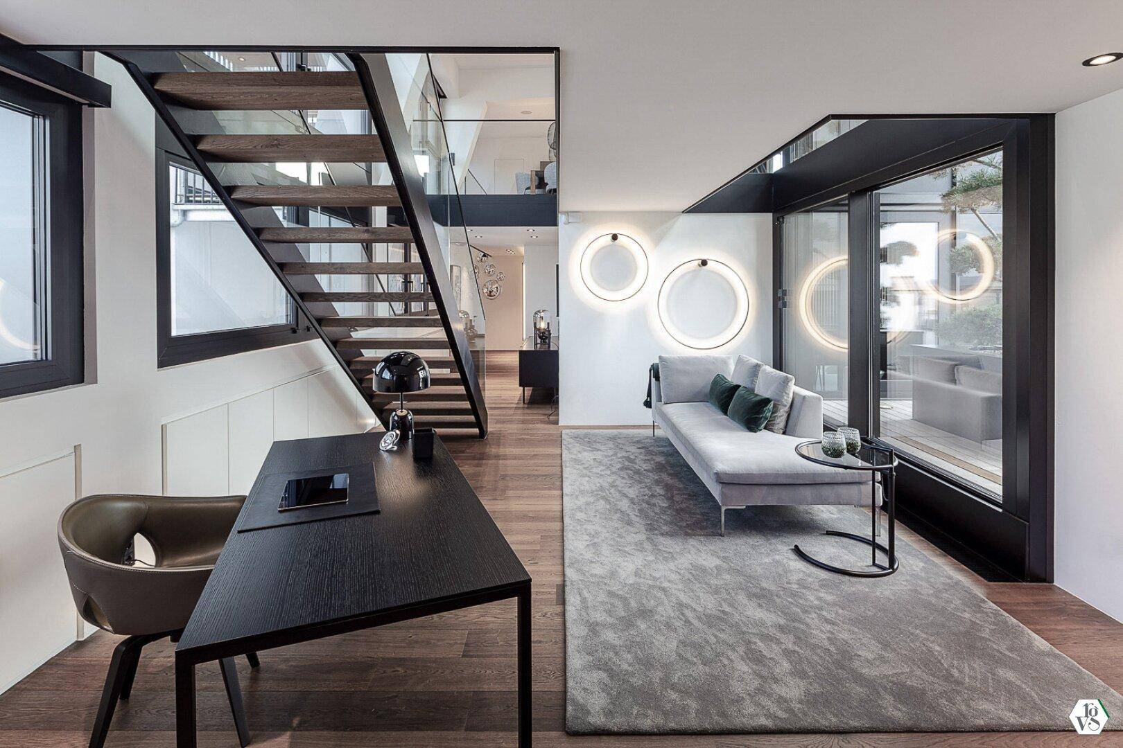 Heller Wohnbereich mit modernem Sofa, Schreibtisch und offener Treppe.