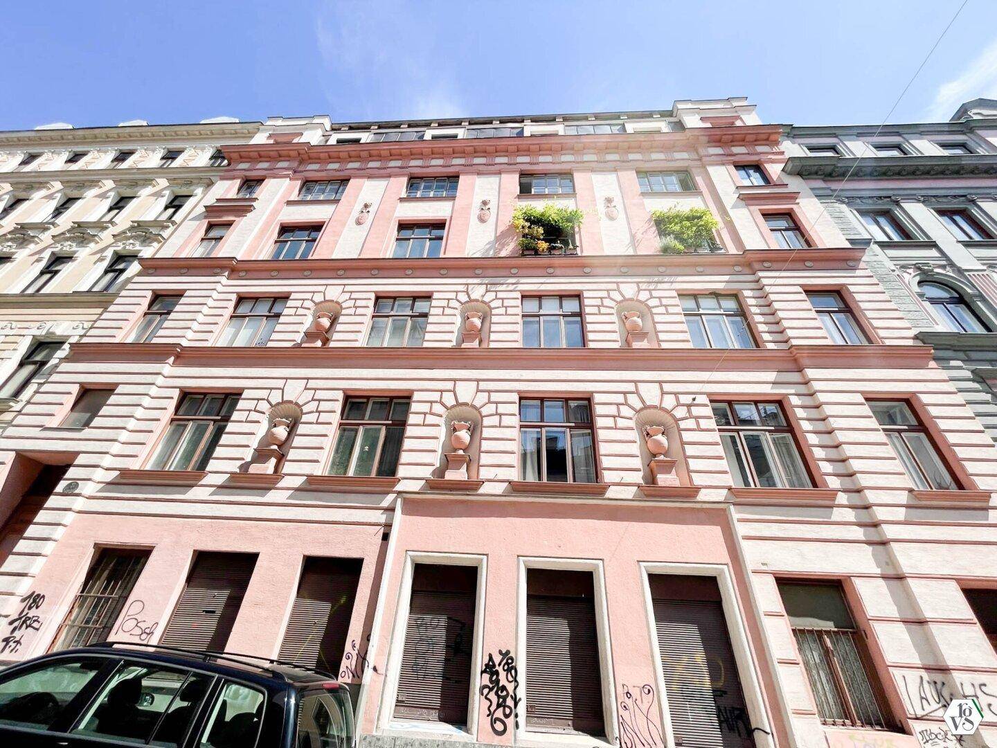 Historische Altbaufassade in Rosa mit vielen Fenstern und dekorativen Elementen.