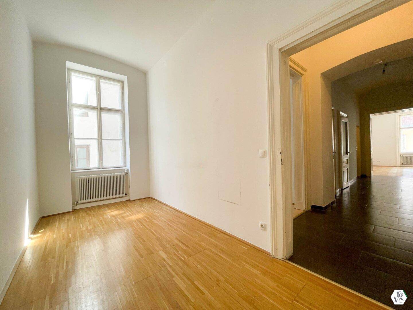 Heller Wohnraum mit Parkettboden und Blick in den gefliesten Flur, typisch für Altbauwohnungen.