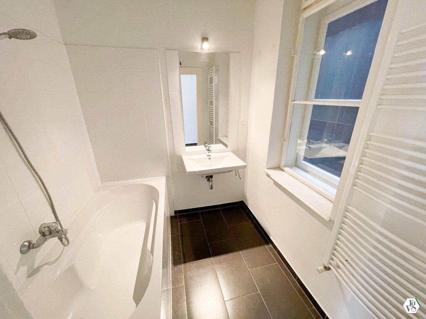 Helles Badezimmer mit Badewanne, Einzelwaschbecken und Fenster für natürliche Belüftung.