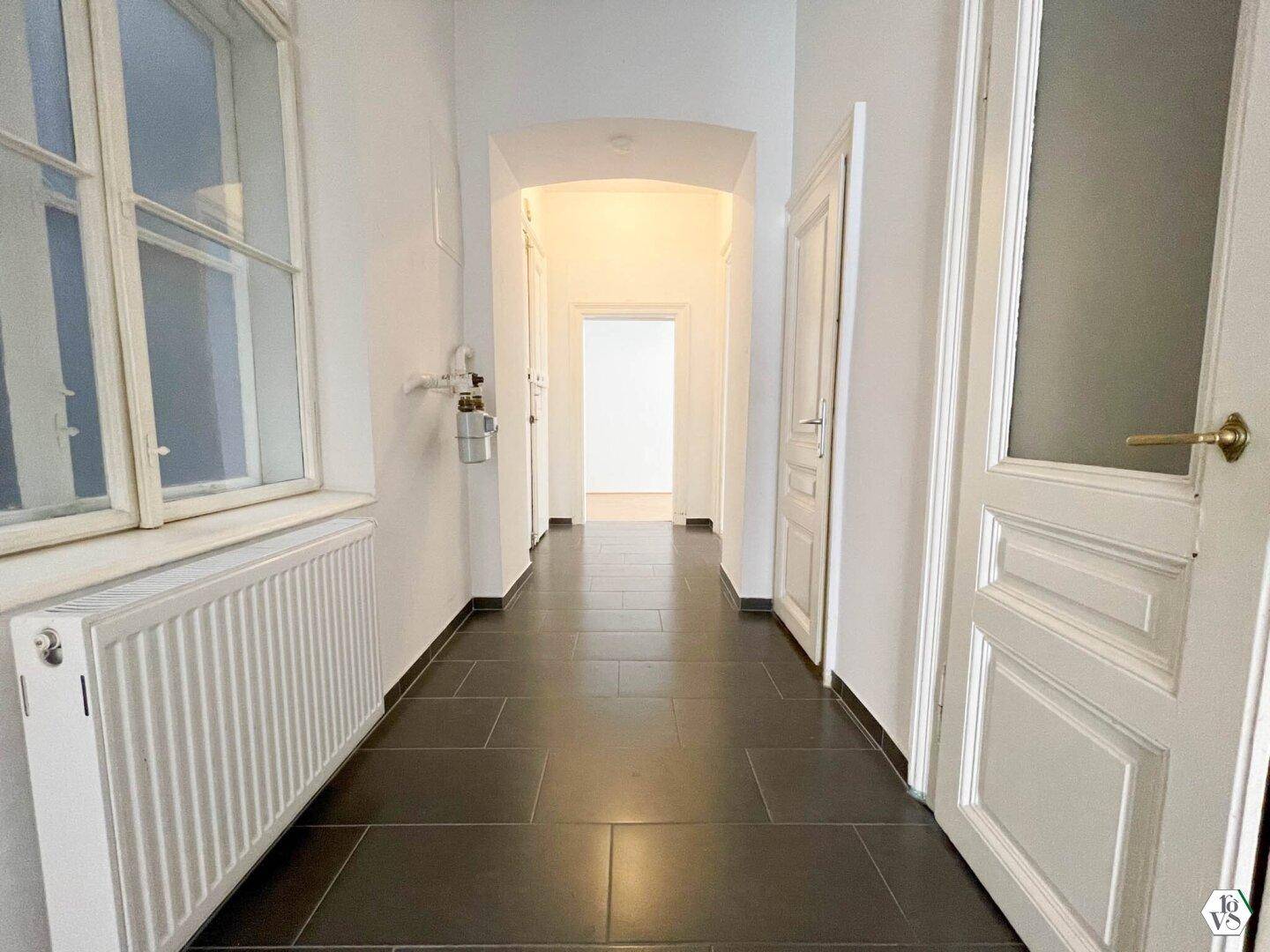 Langer Flur mit dunklen Fliesen und hohen Türen, der die verschiedenen Räume der Wohnung verbindet.