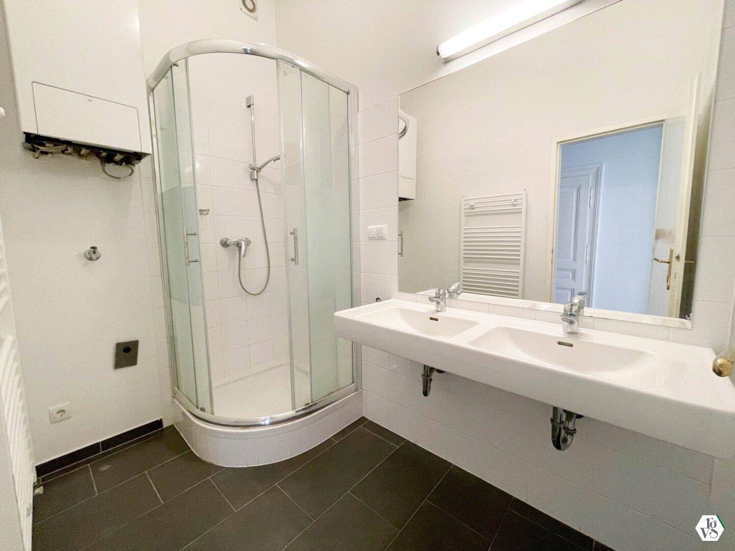Modernes Badezimmer mit Doppelwaschbecken, Duschkabine und dunklen Bodenfliesen.