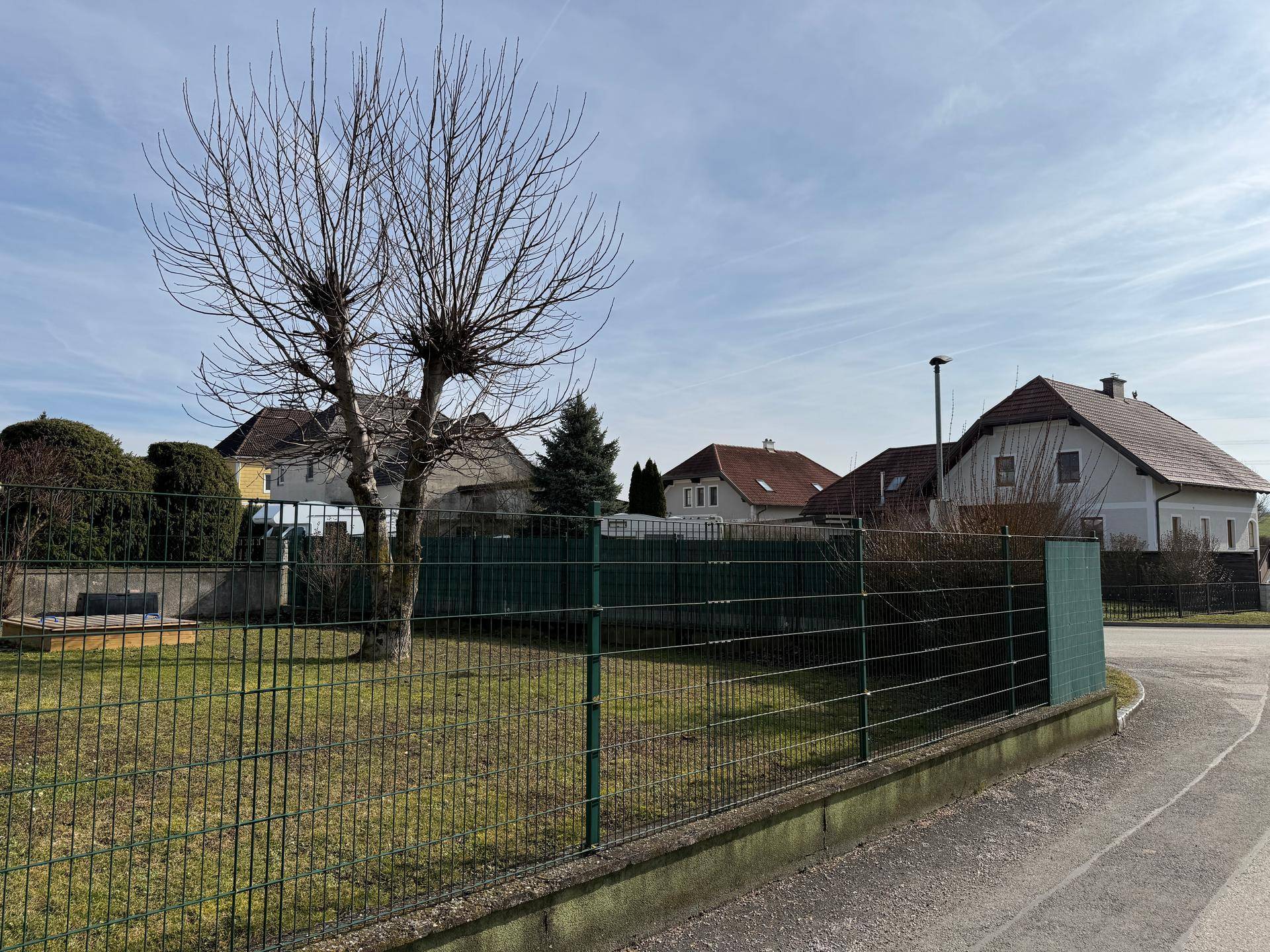 Gartenbereich mit Rasenfläche, Drahtzaun und kahlen Bäumen in ländlicher Umgebung.