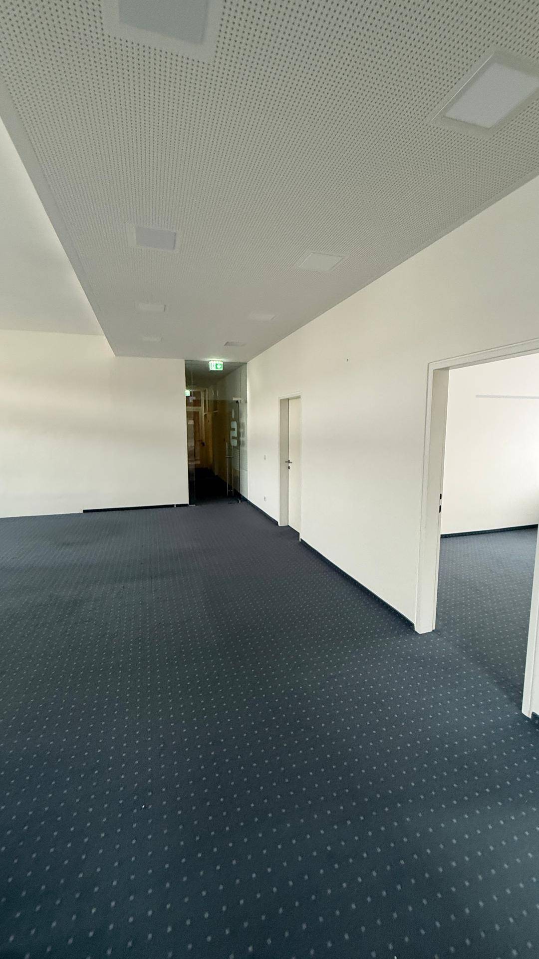 Langer Flur oder offener Bürobereich mit Teppichboden und abgehängter Decke mit Beleuchtung.