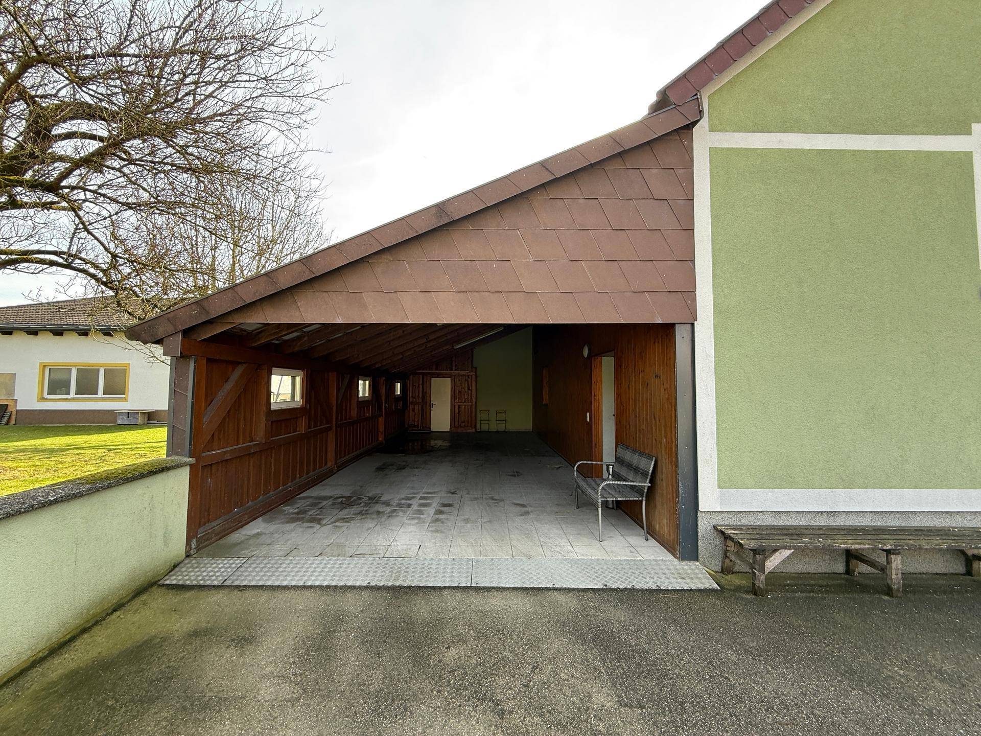 Geräumiger Holzcarport mit Ziegeldach und Sitzbank neben dem Wohnhaus.