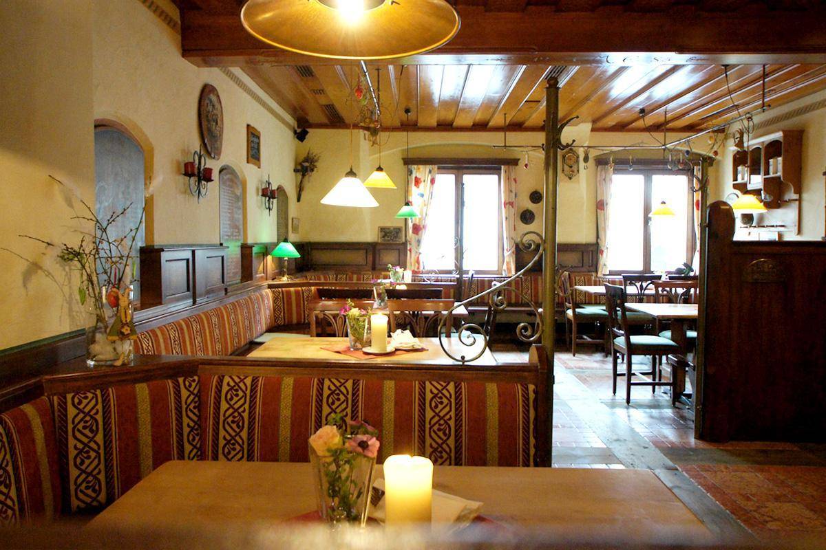Gemütlicher Restaurantbereich im traditionellen Stil mit Holzbalkendecke, gepolsterten Bänken und kleinen Fenstern.
