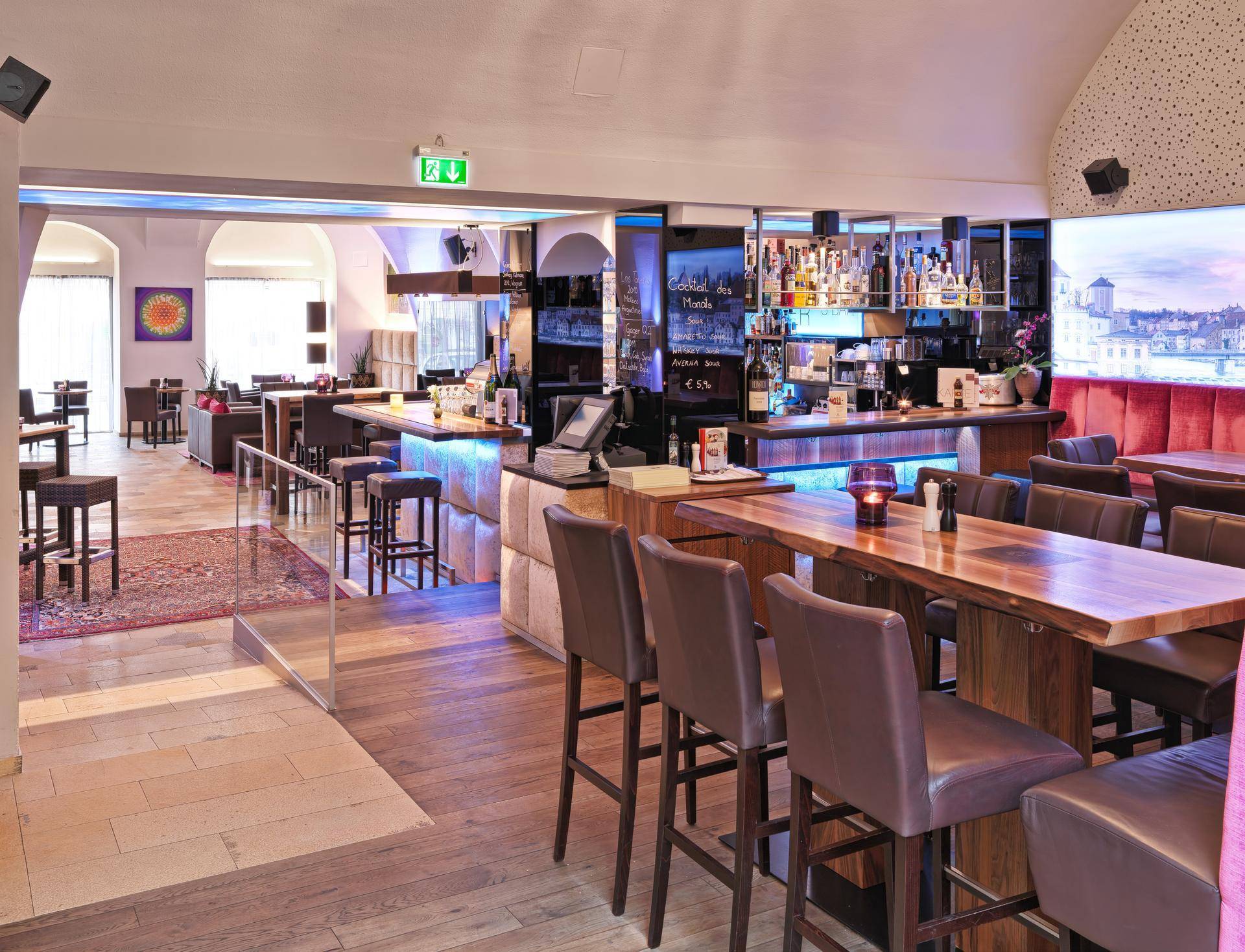Moderne Bar und Lounge-Bereich mit Holzböden, bequemen Sitzgelegenheiten und einer beleuchteten Wanddekoration.