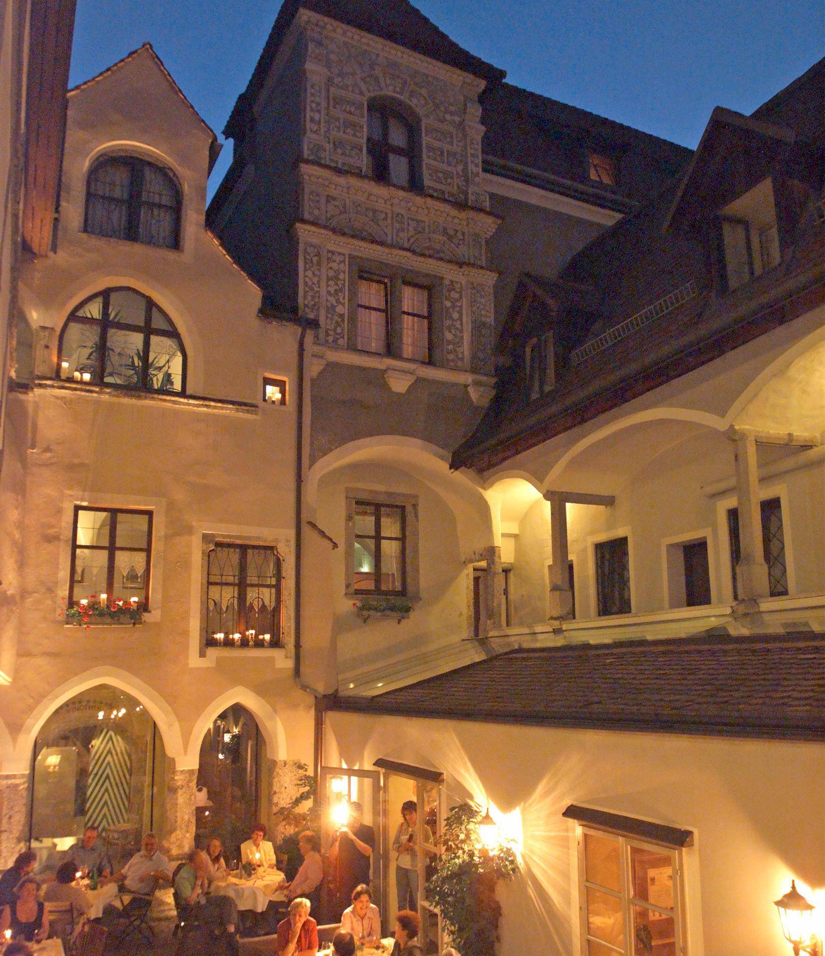 Historischer Innenhof eines Gebäudes am Abend, beleuchtet mit Gästen an Tischen und traditioneller Architektur.