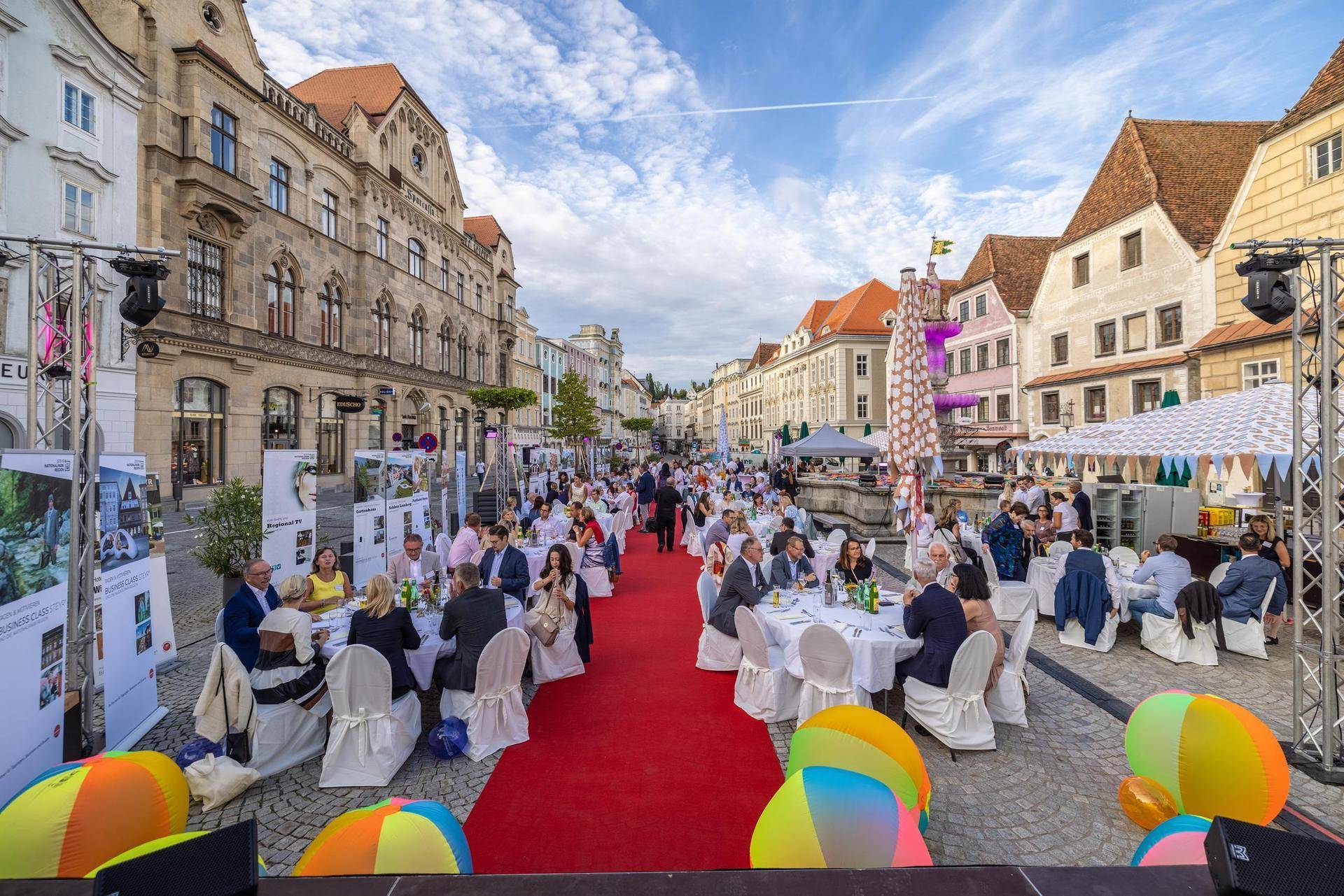 Festlich gedeckte Tische auf einem Stadtplatz für eine Veranstaltung, umgeben von historischen Gebäuden.