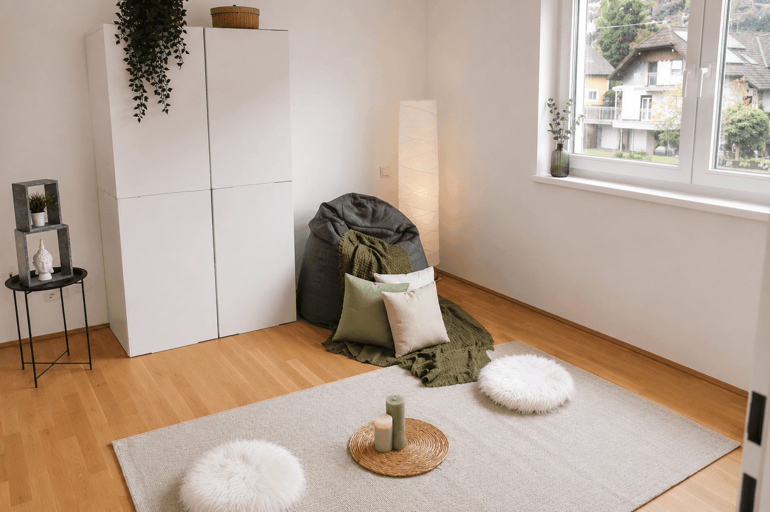 Gemütlicher Wohnbereich mit Holzboden, großem Fenster und weichen Sitzgelegenheiten.