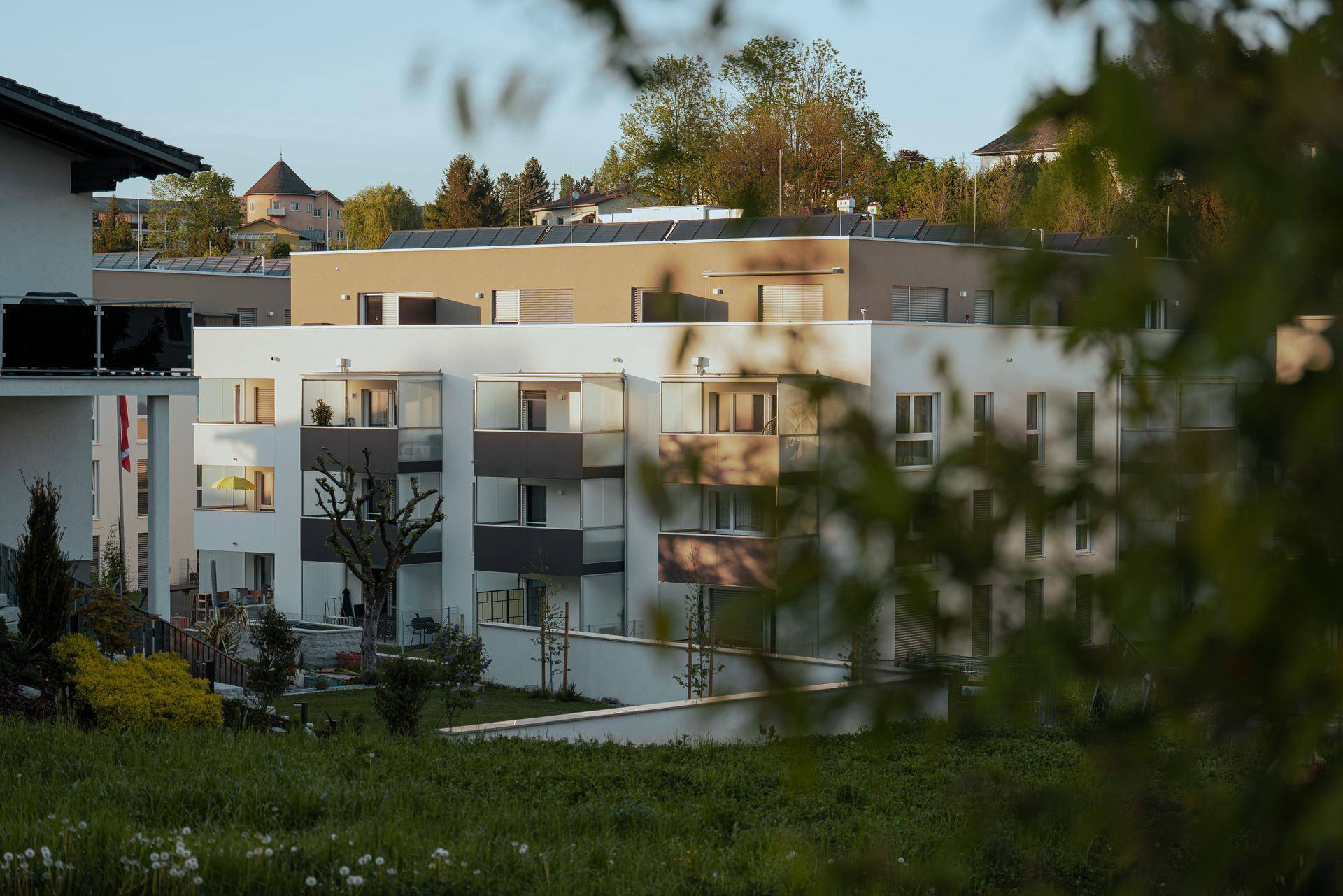 Moderne Wohngebäude mit Balkonen und Flachdächern, umgeben von grüner Landschaft.