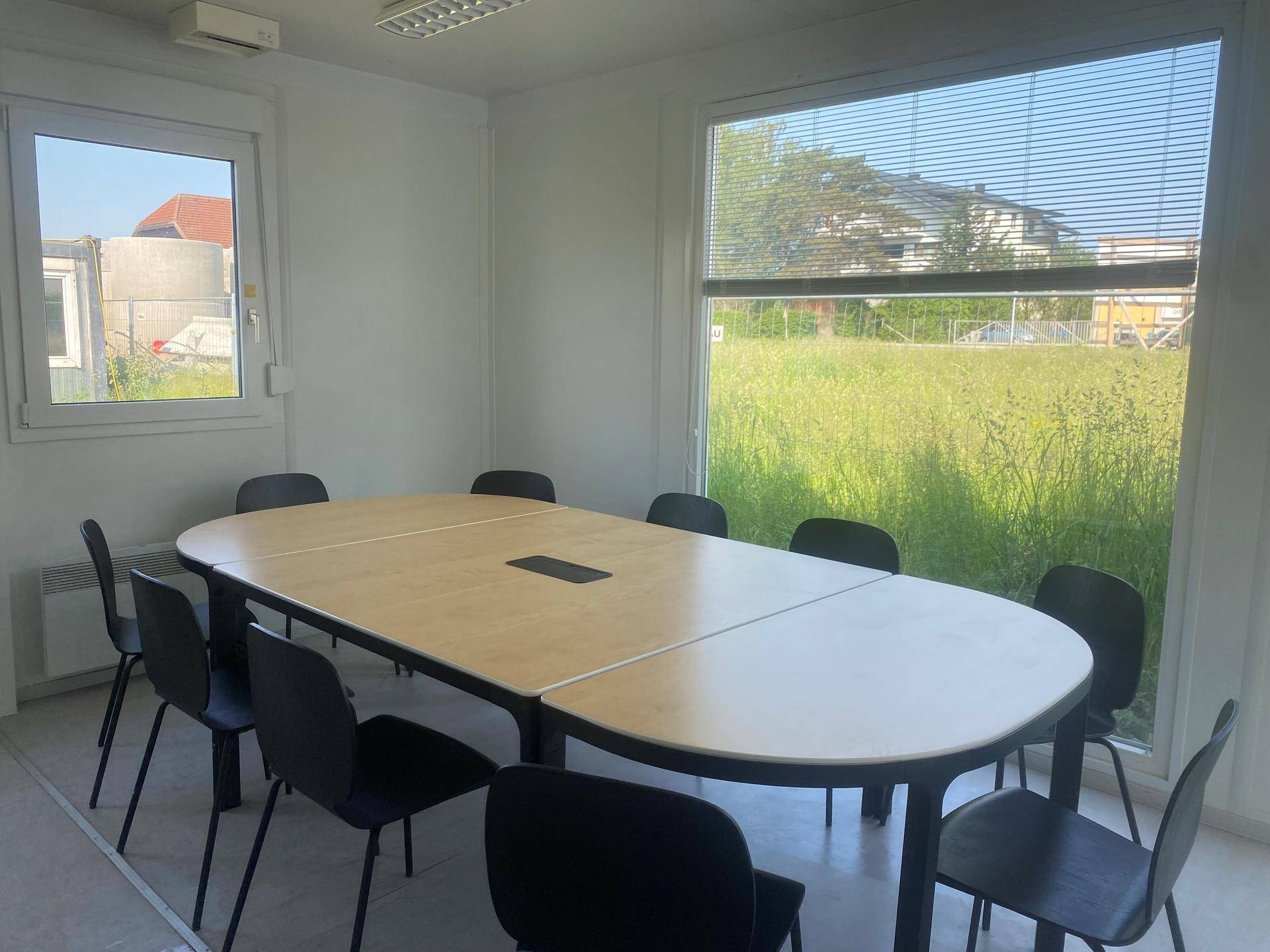 Geräumiger Bürobereich mit langem Konferenztisch und Blick auf eine grüne Wiese durch das große Fenster.