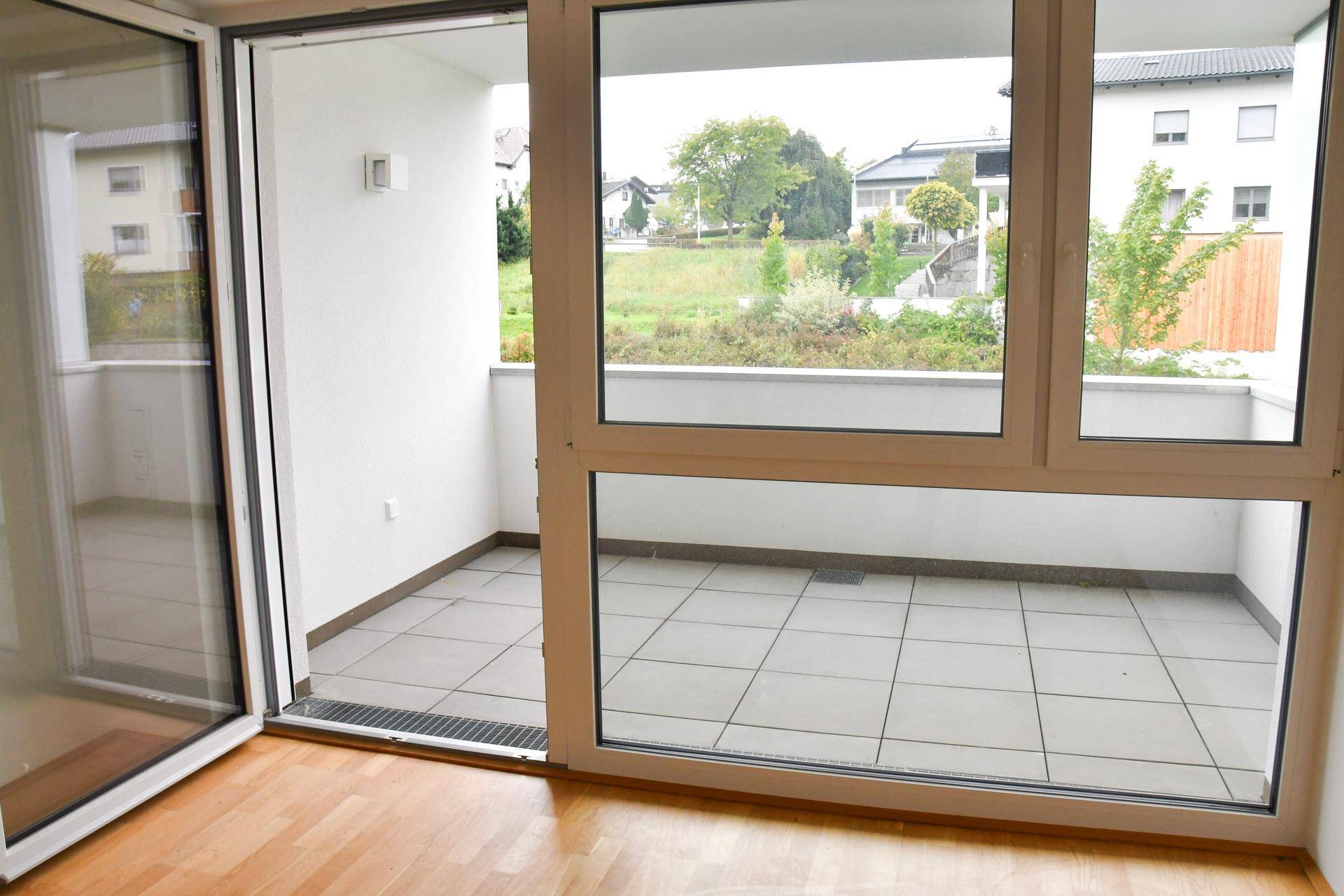 Heller Balkon mit Fliesenboden und Blick ins Grüne, zugänglich durch eine große Glasschiebetür.
