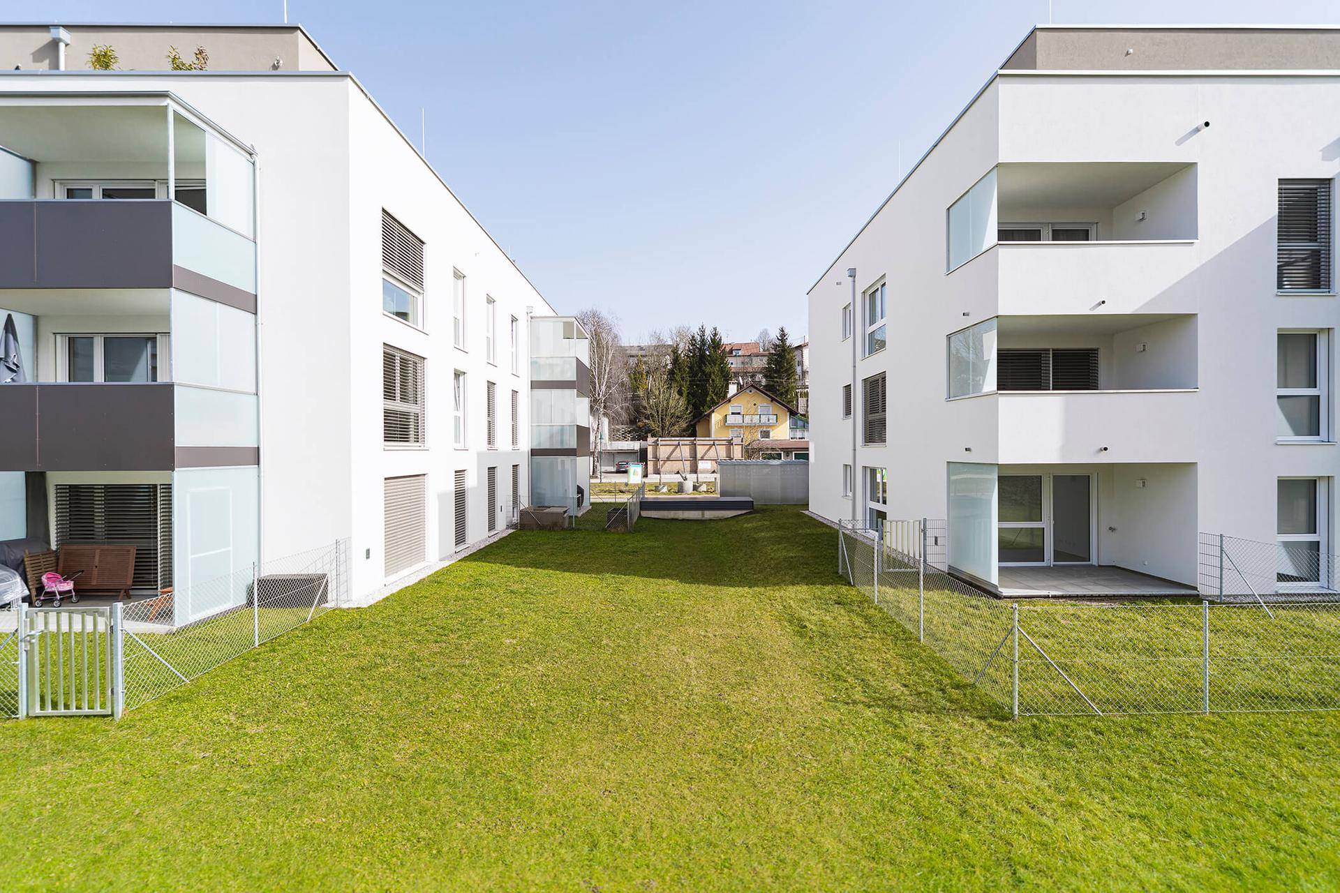Gemeinschaftlicher Gartenbereich zwischen modernen Wohngebäuden mit gepflegtem Rasen.
