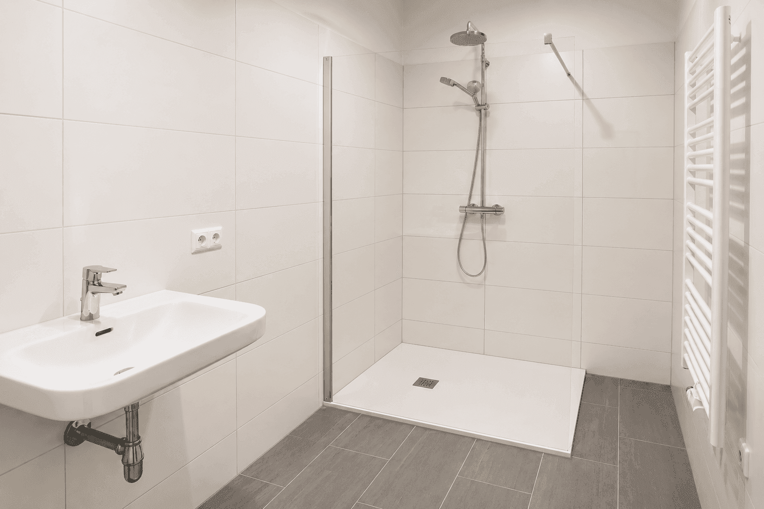 Modernes Badezimmer mit weißen Fliesen, ebenerdiger Dusche, Waschbecken und beheiztem Handtuchhalter.