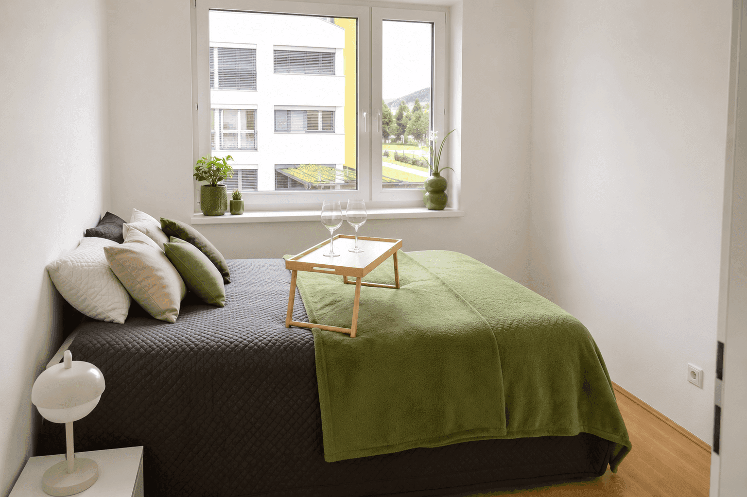 Helles Schlafzimmer mit Holzboden, großem Fenster und grünen Akzenten.