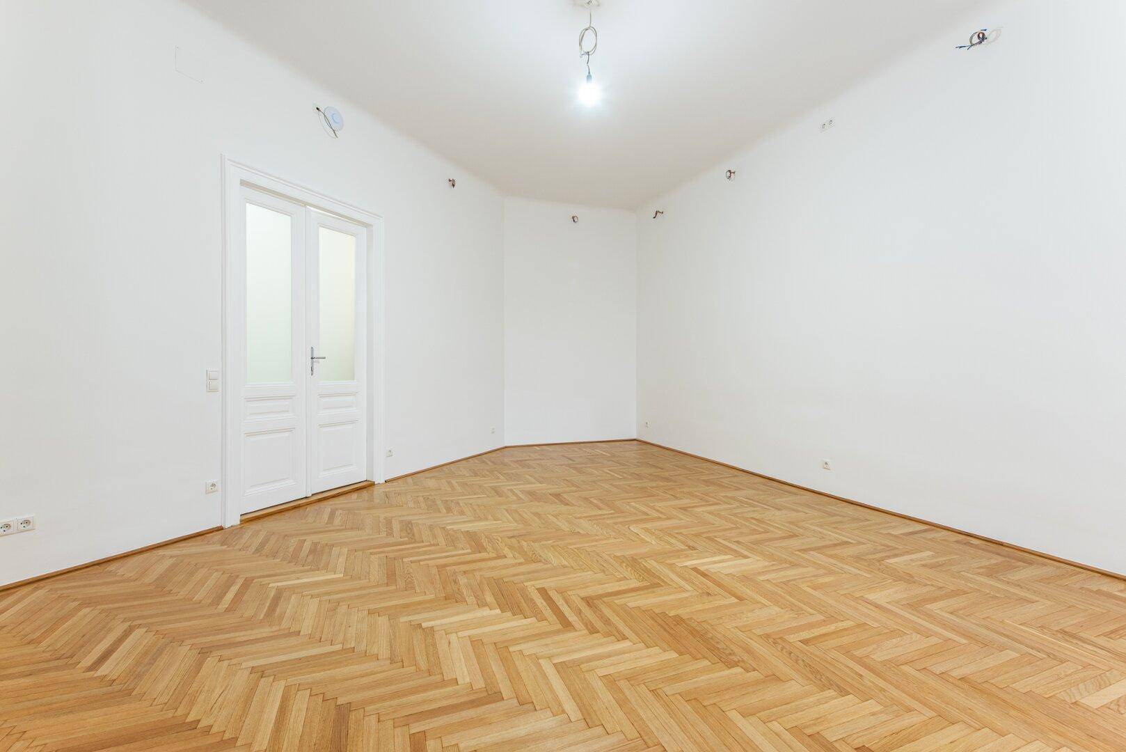 Großer, heller Raum mit Fischgrätparkett und einer Doppeltür.