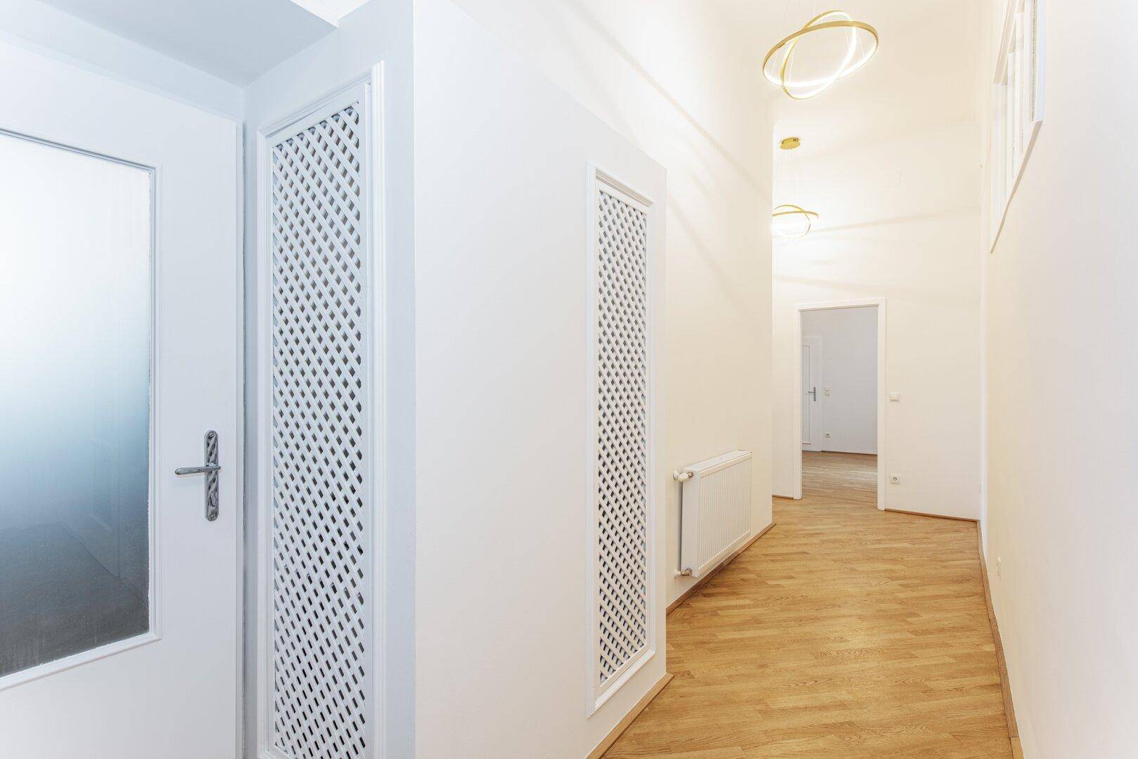 Heller Flur mit Fischgrätparkett, weißen Wänden und dekorativen Heizkörperverkleidungen.