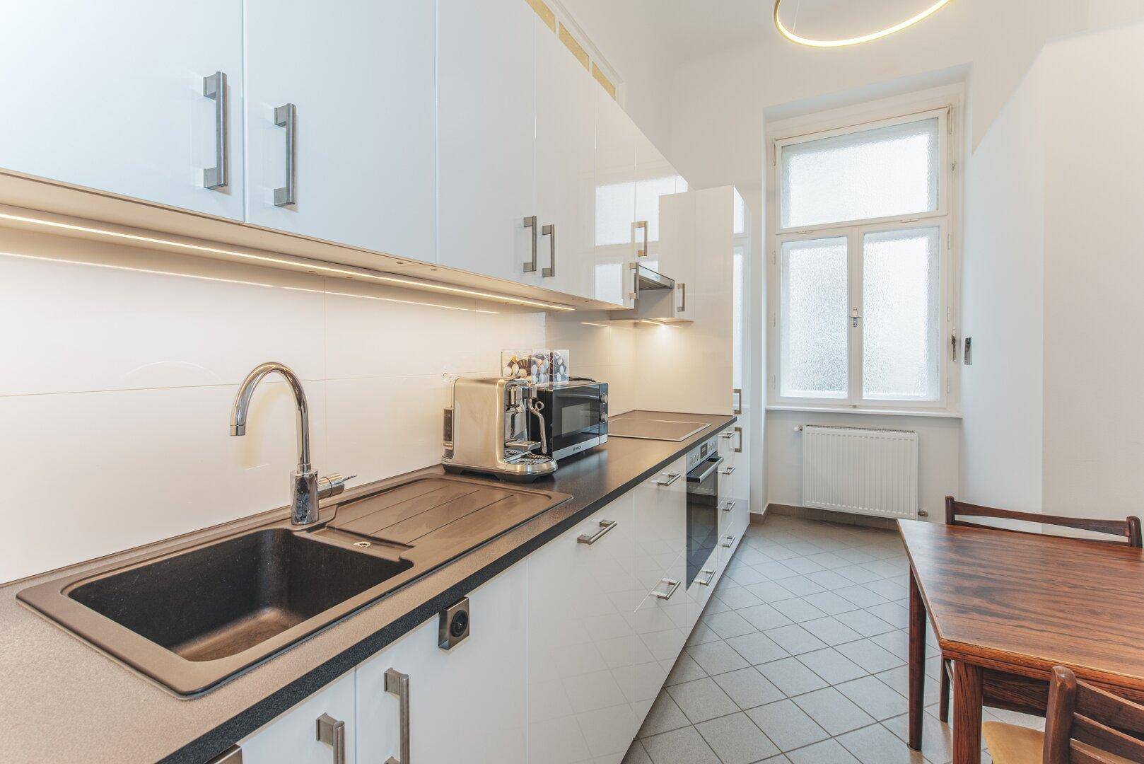 Moderne Küche mit weißen Schränken, dunkler Arbeitsplatte und Essbereich am Fenster.