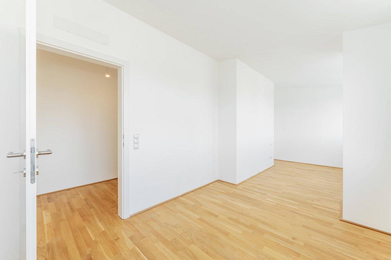 Leerer, heller Raum mit Holzboden und weißen Wänden, bereit für individuelle Gestaltung.