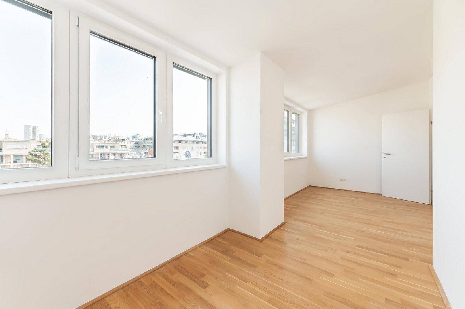 Heller, leerer Raum mit Holzboden und großen Fenstern, die einen weiten Blick über die Stadt bieten.