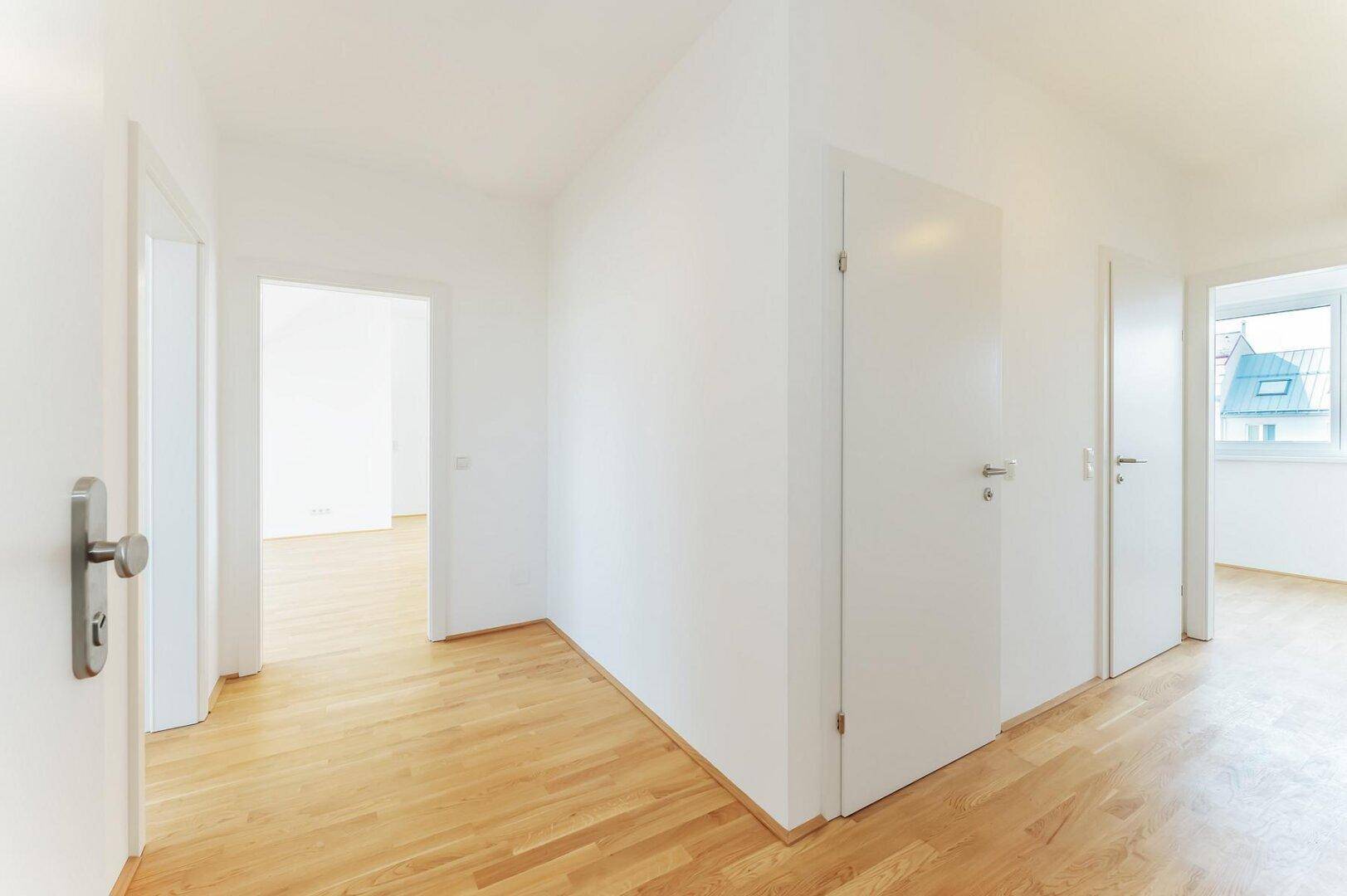 Heller Flur mit Holzboden und mehreren weißen Türen, der verschiedene Räume miteinander verbindet.