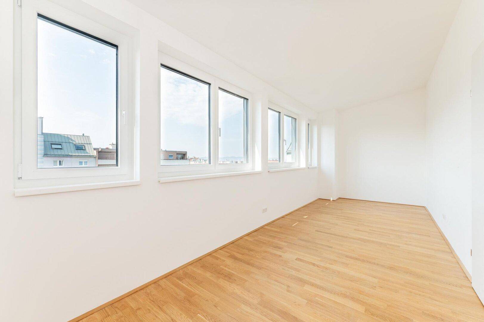 Geräumiger, heller Raum mit Holzboden und einer Fensterfront, die einen weiten Stadtblick ermöglicht.