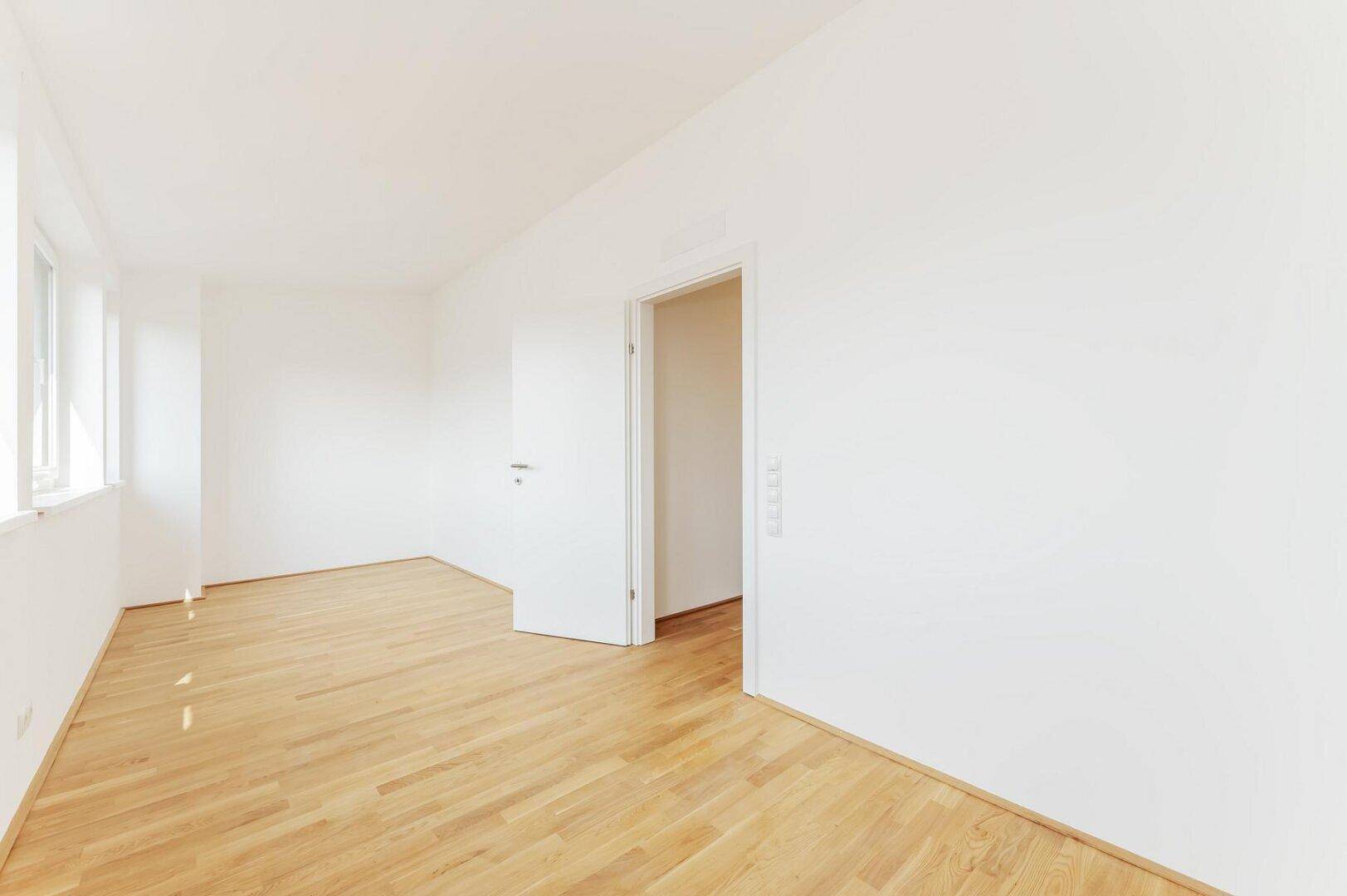 Lichtdurchfluteter, leerer Raum mit Holzboden und weißen Wänden, ideal für vielfältige Nutzung.