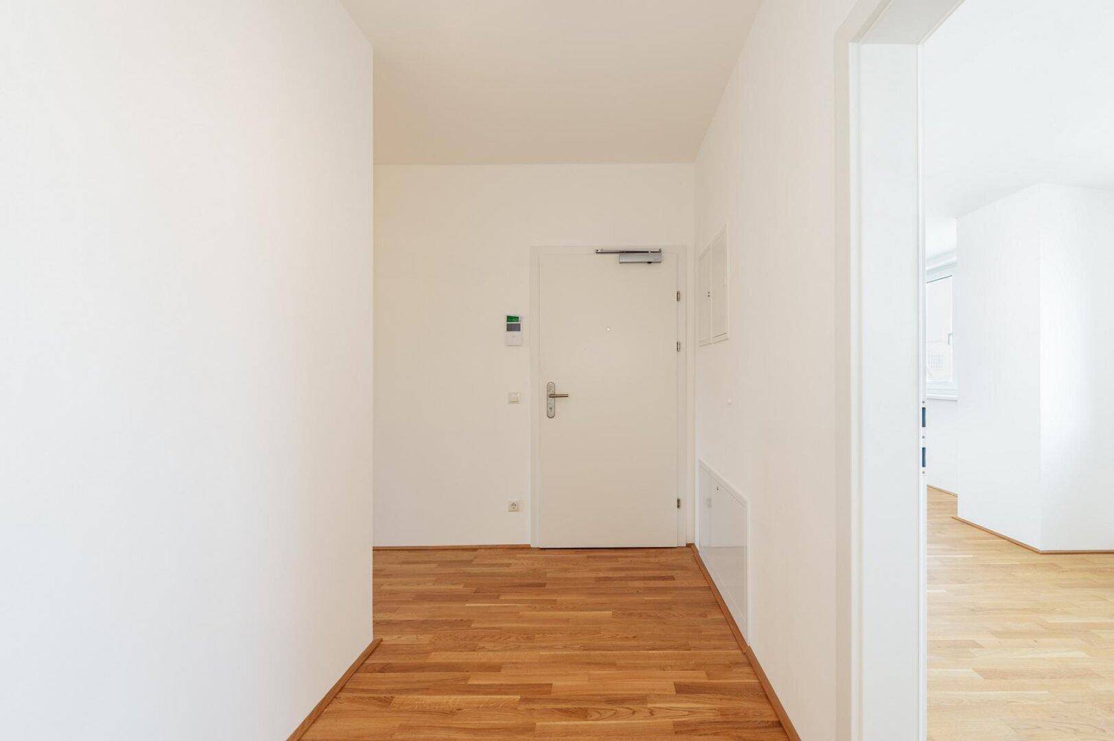 Heller Eingangsbereich mit Holzboden und weißer Eingangstür, der einen freundlichen Empfang bietet.